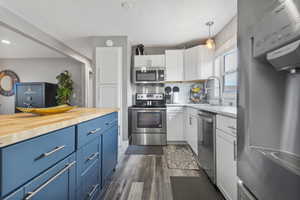 Kitchen featuring a blue-painted island with a wood countertop, white cabinetry, stainless steel appliances, and wood-finish flooring