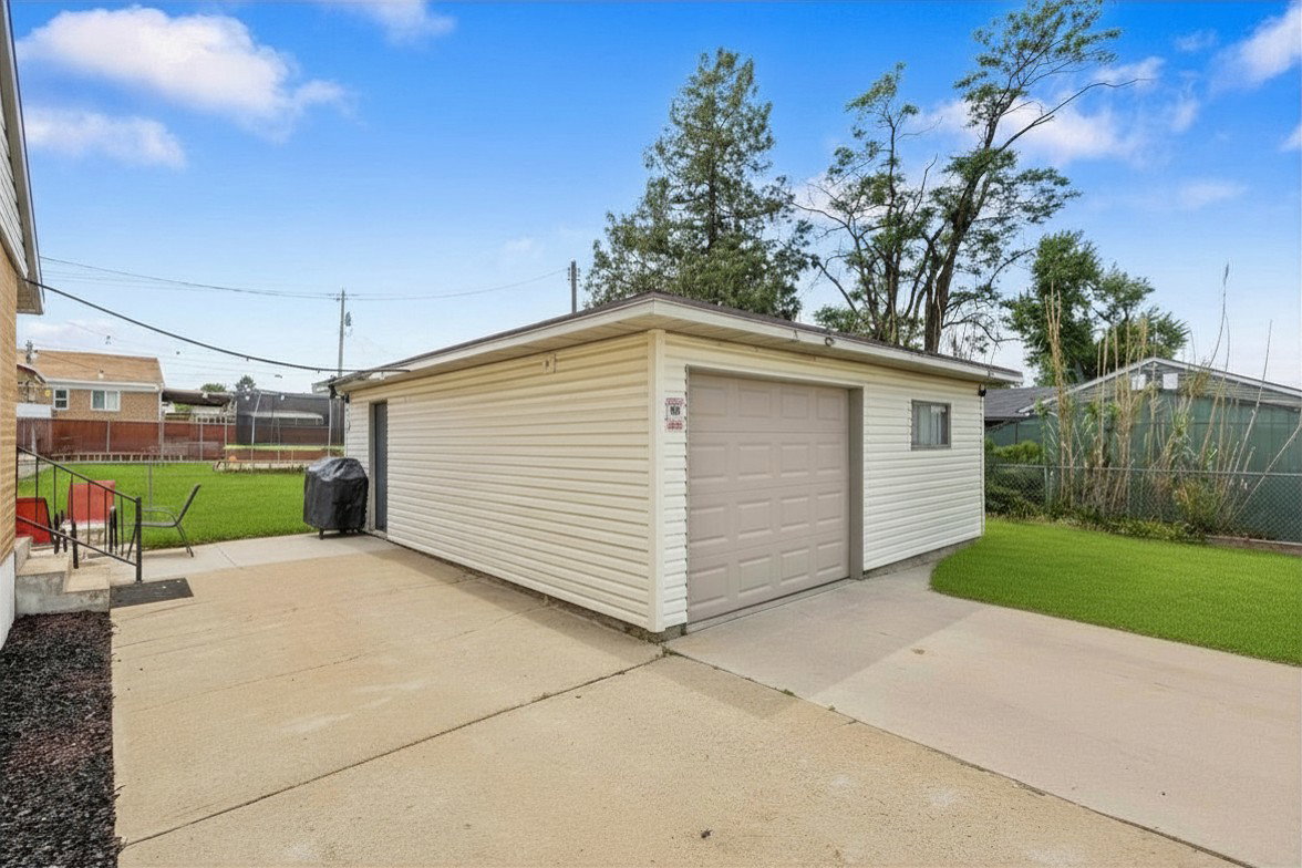 Detached garage with siding exterior and an overhead door, accompanied by a concrete driveway
