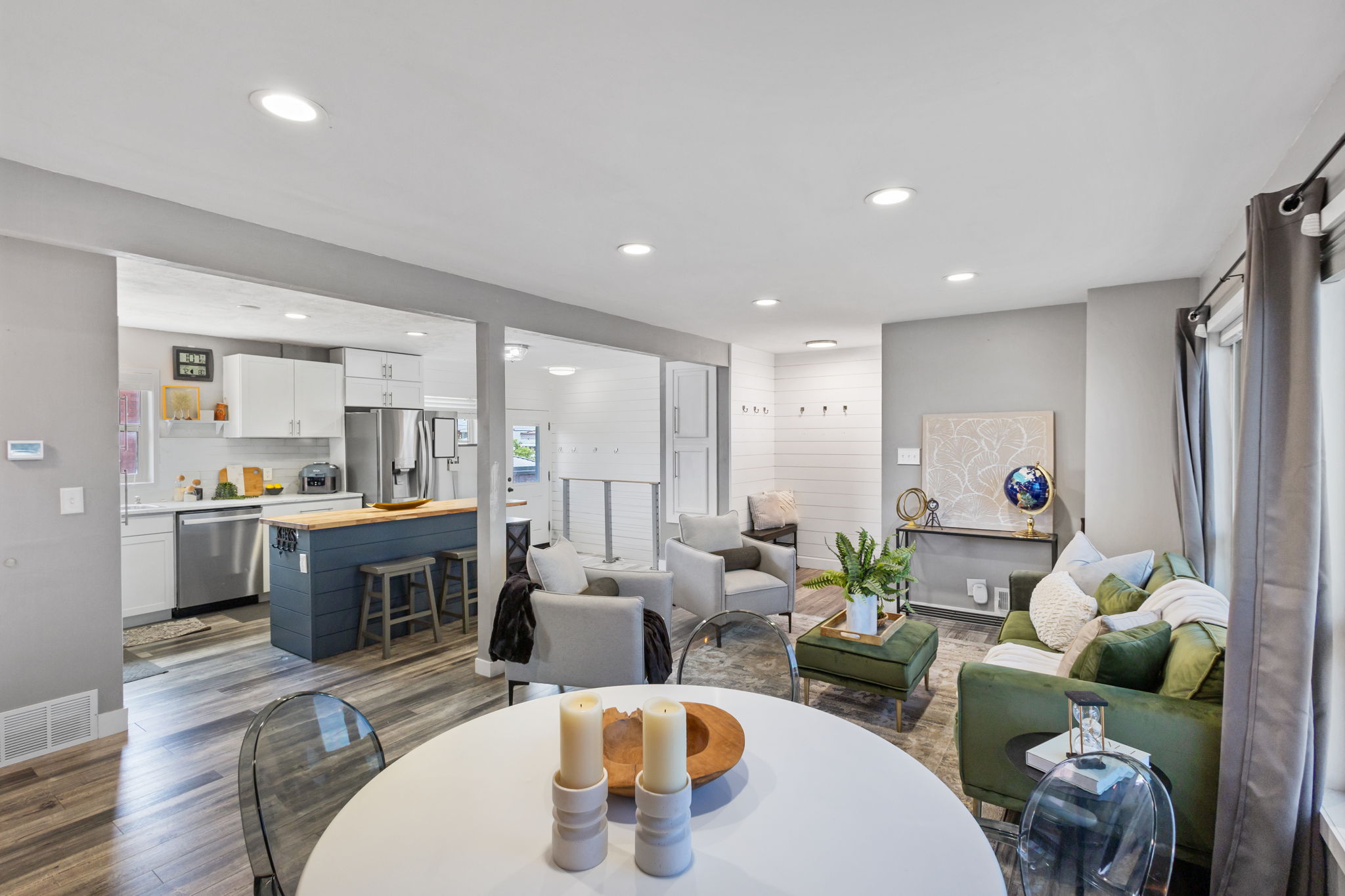 Open-concept main living area with wood-finish flooring, recessed lighting, and a kitchen featuring white cabinetry, a blue island with a wood countertop, and stainless steel appliances
