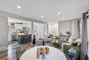 Open-concept main living area with wood-finish flooring, recessed lighting, and a kitchen featuring white cabinetry, a blue island with a wood countertop, and stainless steel appliances