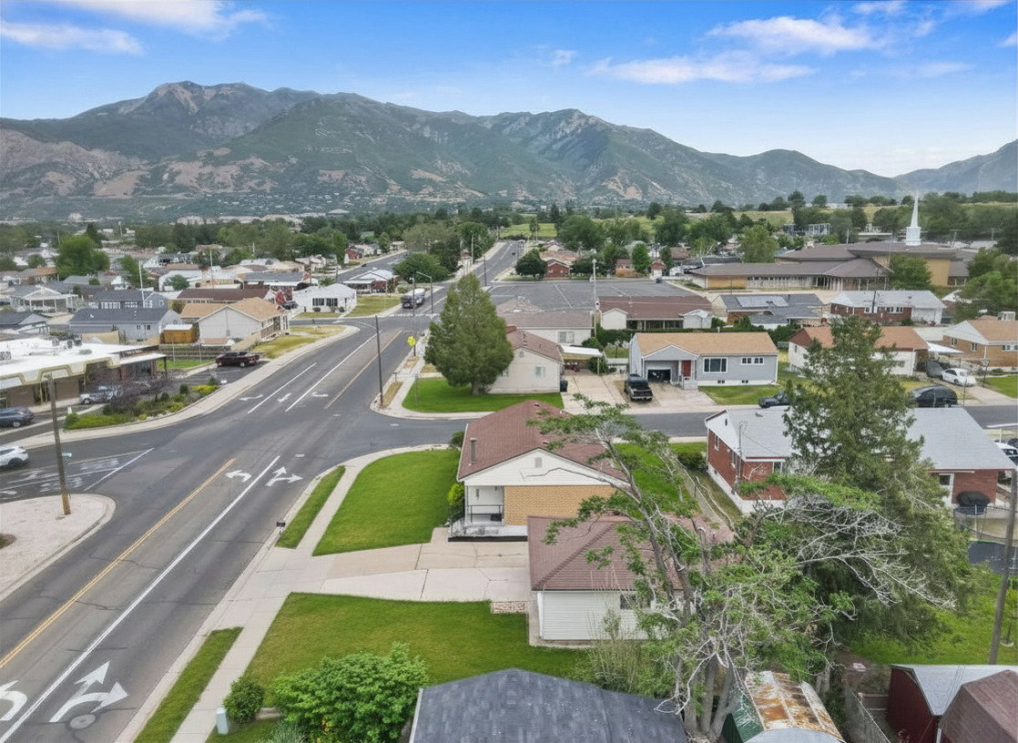 Neighborhood aerial featuring residential properties with mountain backdrop, established landscaping, and paved streets