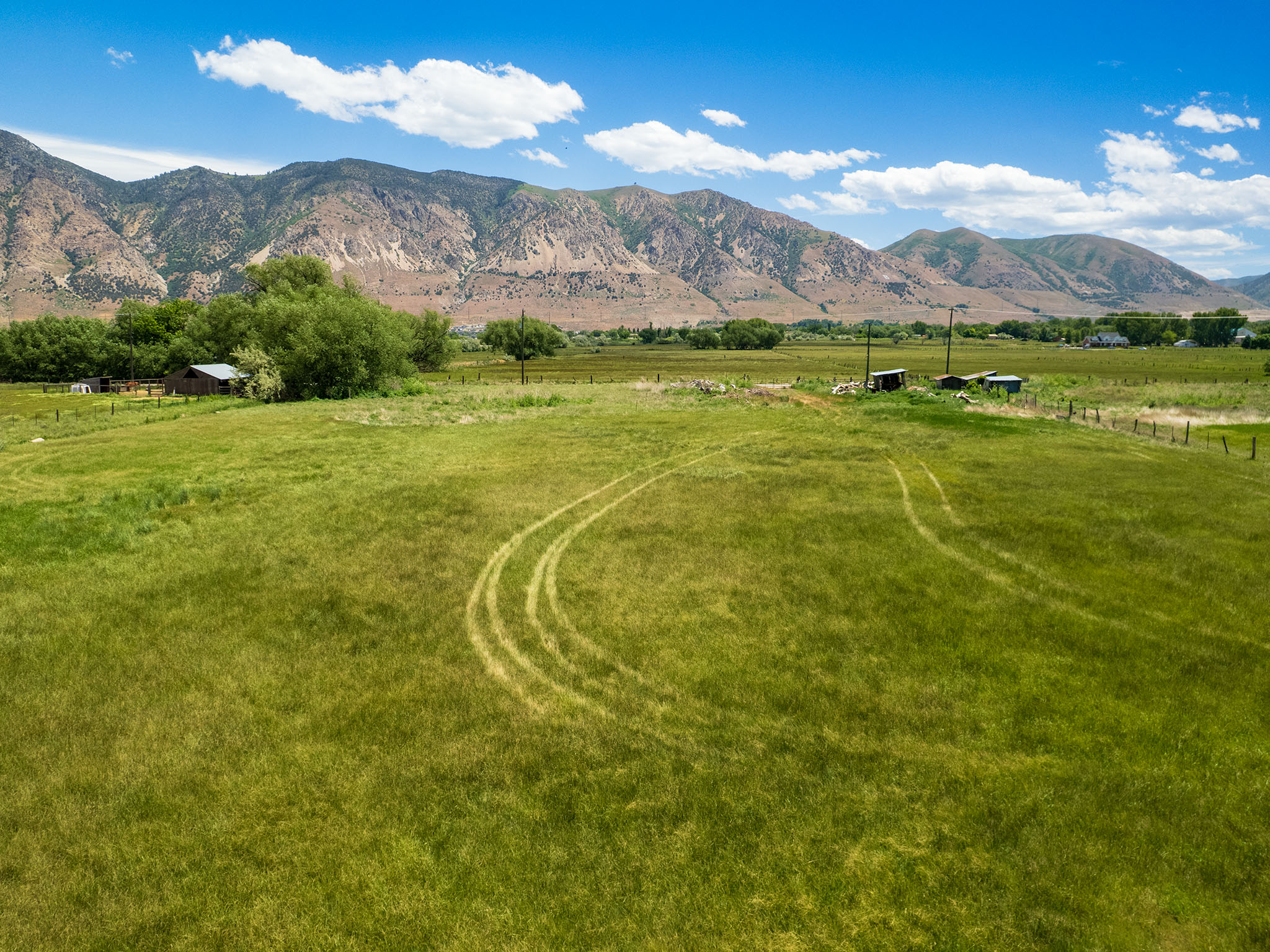 Expansive green field with mountain backdrop, offering open land and distant structures