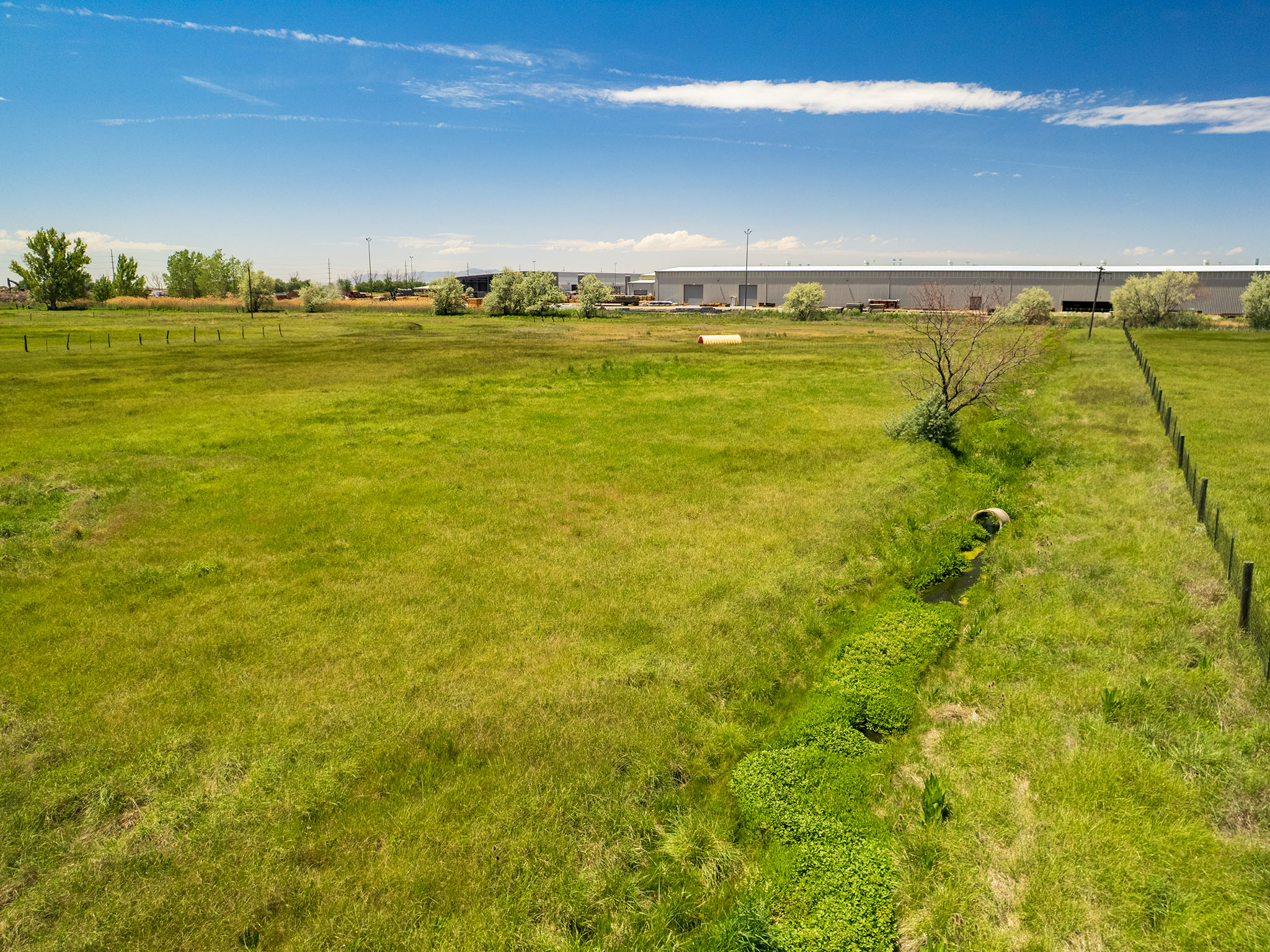 Expansive green field with a natural waterway, bordered by a wire fence