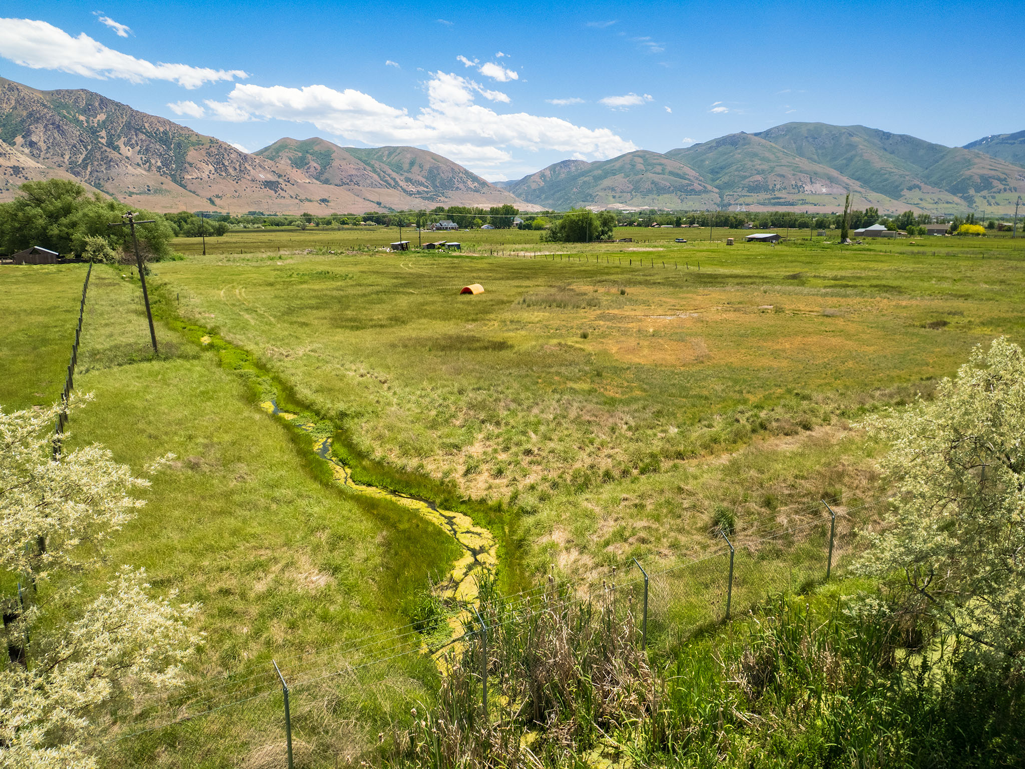 Expansive green field featuring a winding natural water feature, bordered by distant mountains