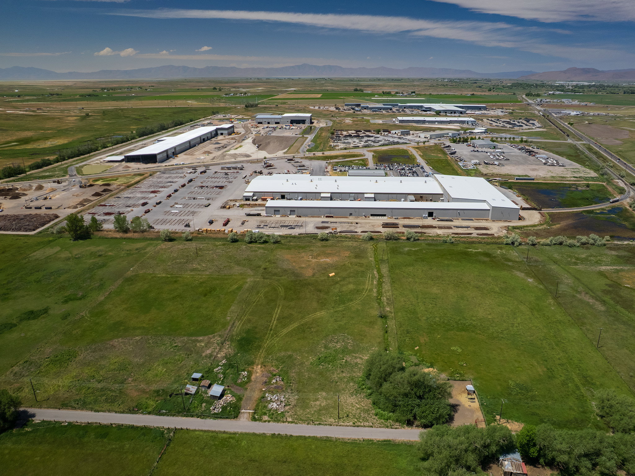 Expansive commercial property featuring multiple large industrial buildings with bright white roofs and extensive paved and unpaved outdoor storage areas