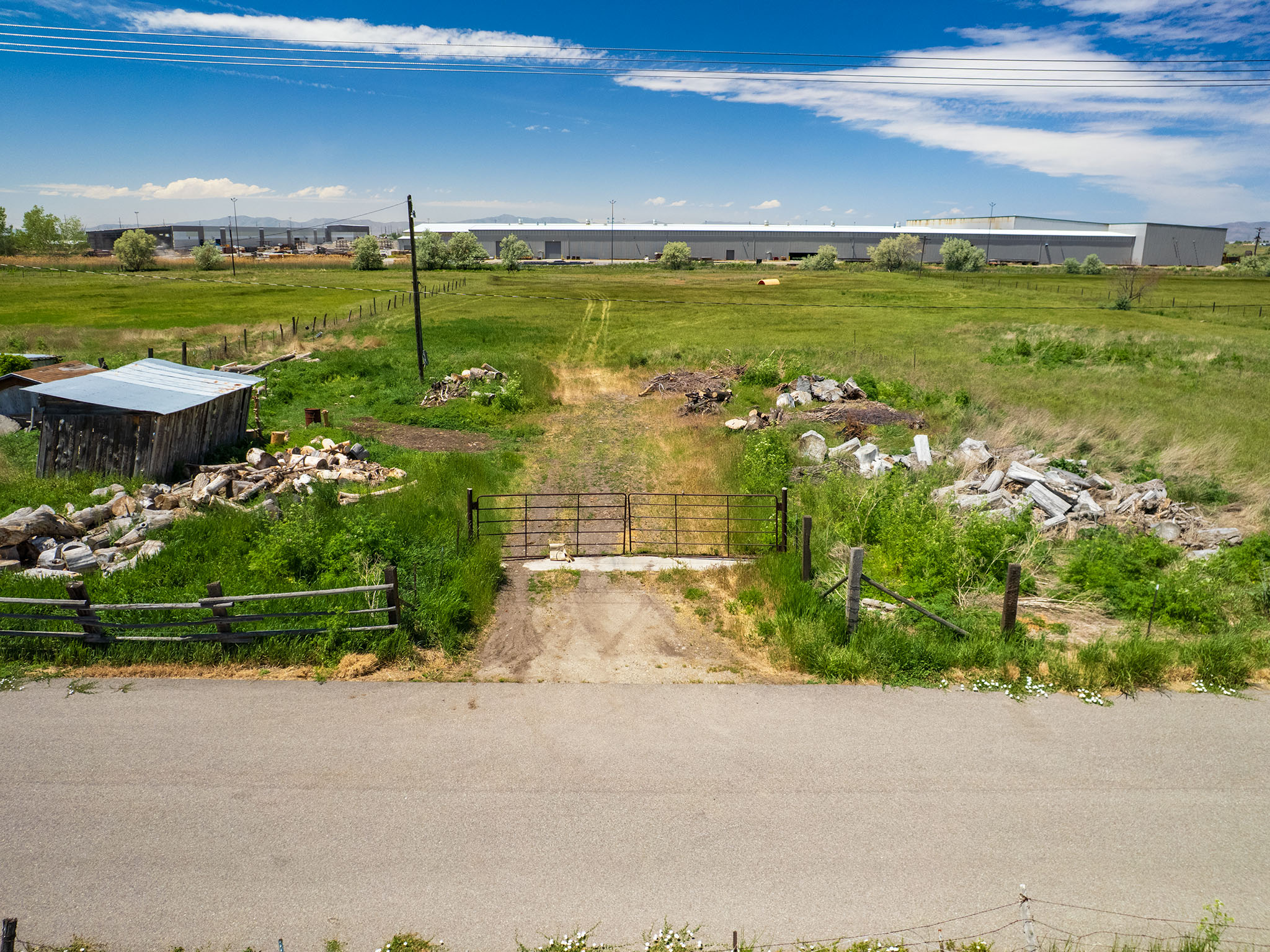 Expansive green field featuring a gravel access path, a metal gate, and a rustic wooden shed