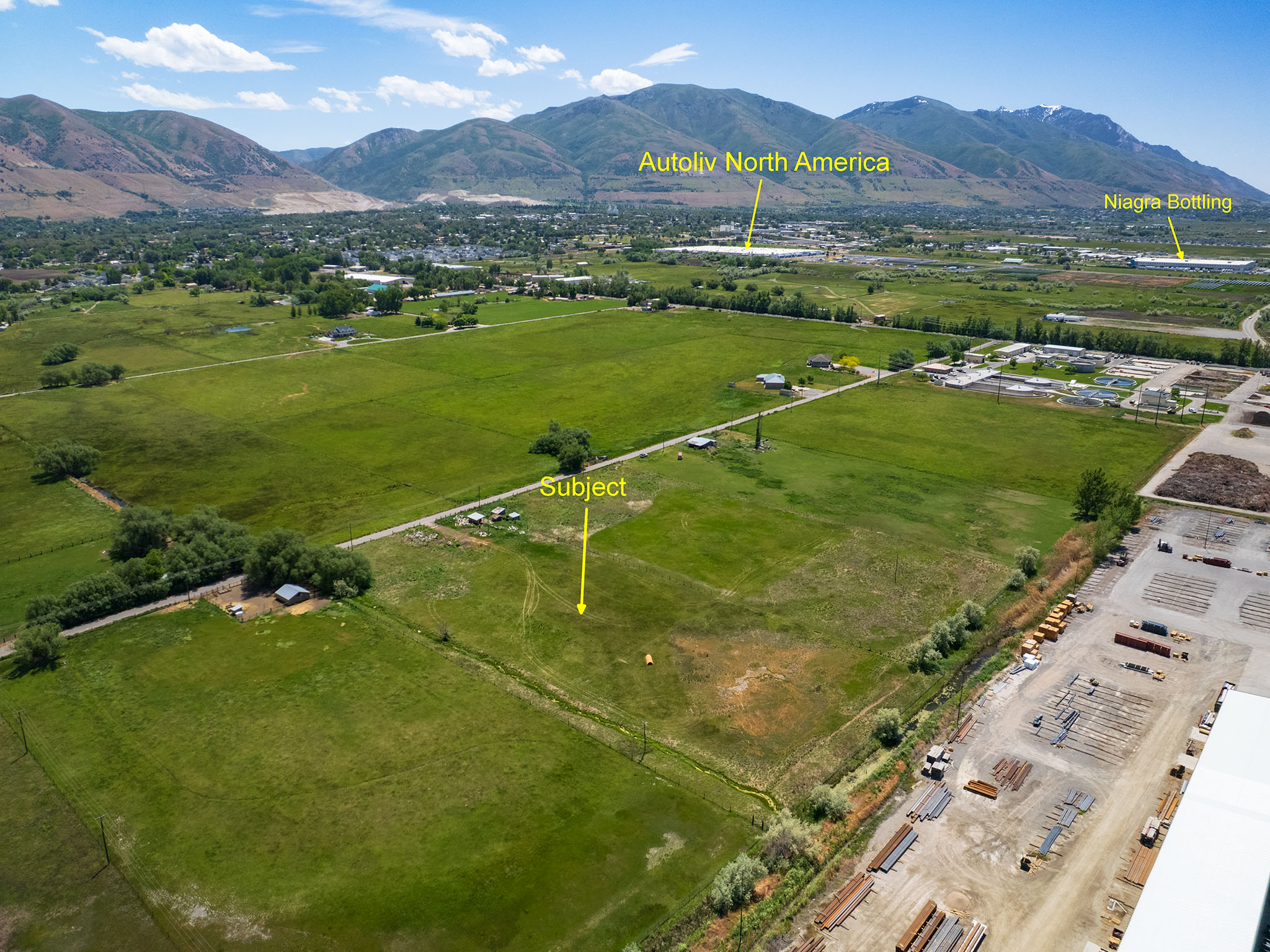 Expansive green acreage featuring a mountainous backdrop, visible roadways, and distant industrial facilities