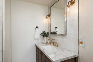Bathroom vanity featuring a natural stone countertop with an undermount sink and brass-finish faucet