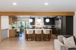 Open-concept kitchen featuring an island with seating, dark green cabinetry, stainless steel appliances, and a light wood-finish flooring