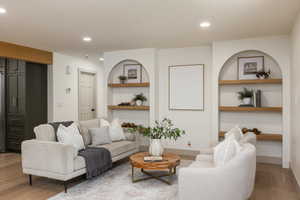 Living area featuring built-in arched alcoves with wood shelving, recessed lighting, and wood-finish flooring