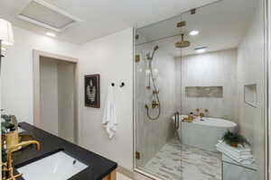 Spacious bathroom featuring a frameless glass shower enclosure, a freestanding oval soaking tub with brass fixtures, and a vanity with a dark countertop and undermount sink