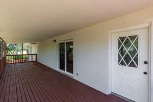 Expansive covered patio featuring wood-finish decking, painted brick exterior, and a white entry door with diamond-patterned lites