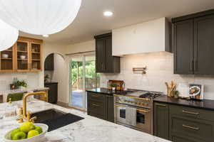 Kitchen featuring dark cabinetry, lighter wood-finish upper cabinets with glass panels, and a white marble-patterned countertop with an undermount sink