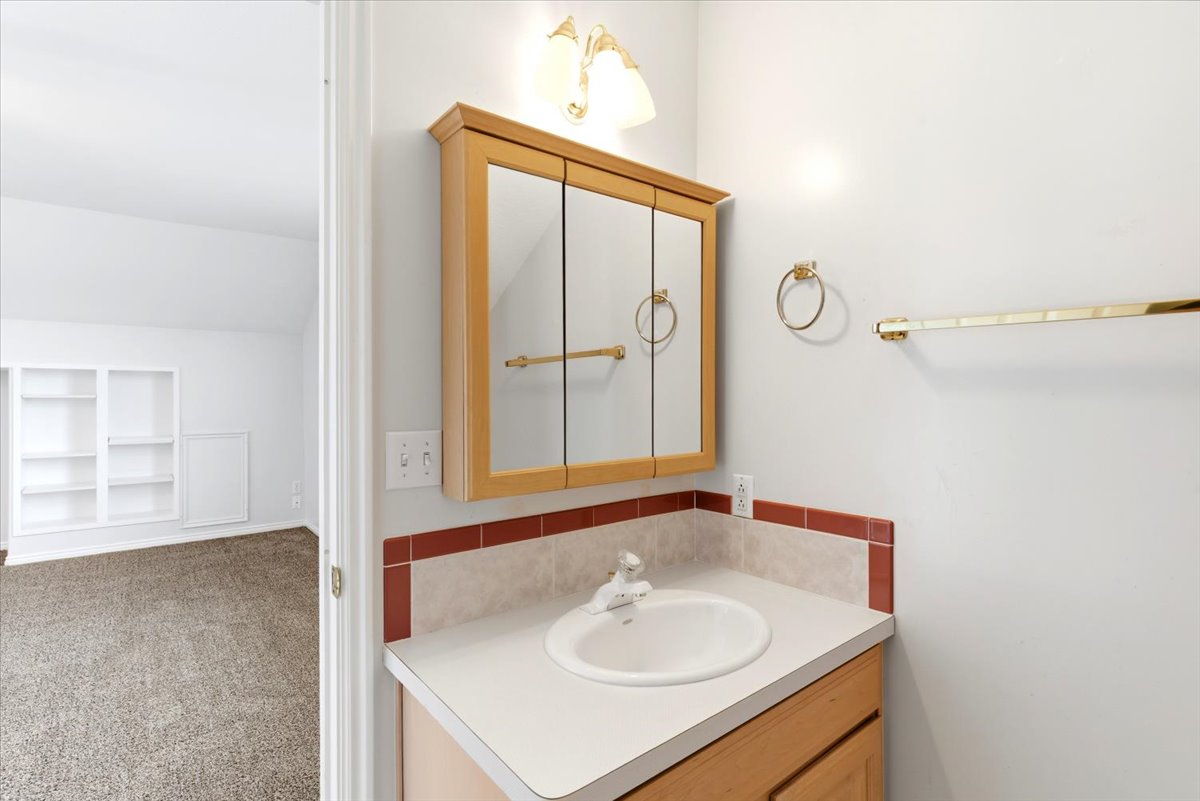Bathroom vanity with a wood-finish cabinet, integrated sink, and laminate countertop featuring a tiled backsplash