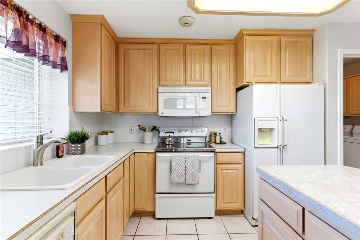 Kitchen featuring wood cabinetry, white appliances, tile flooring, white countertops, and a double basin sink