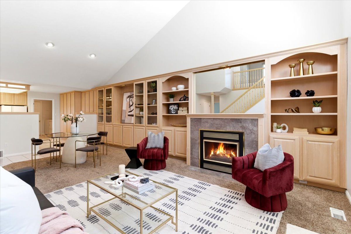 Living area featuring a fireplace with stone surround, built-in shelving, vaulted ceiling, and recessed lighting