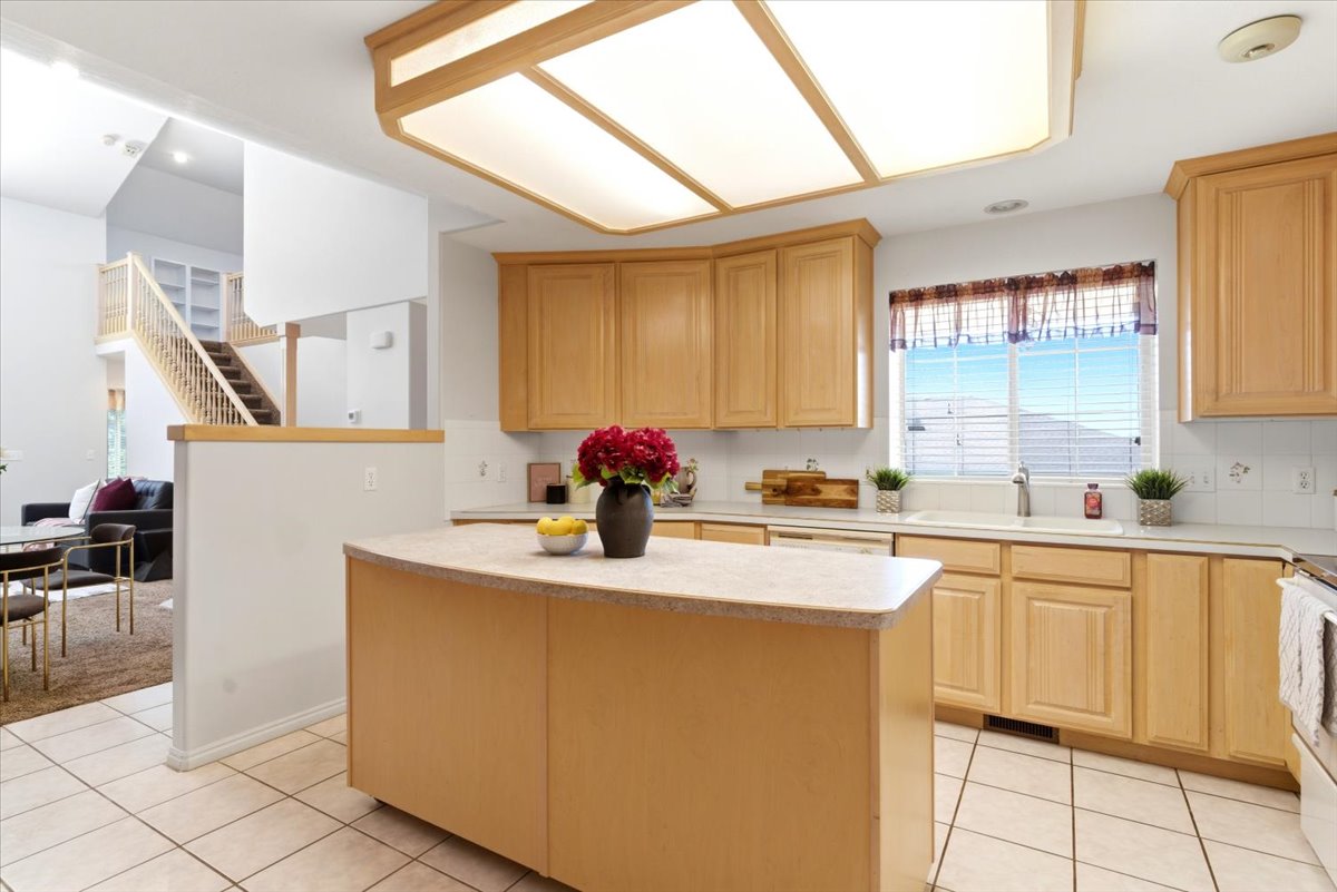 Kitchen featuring a moveable central island with a solid surface countertop, light wood-finish cabinetry, tile flooring, and a large window above the sink