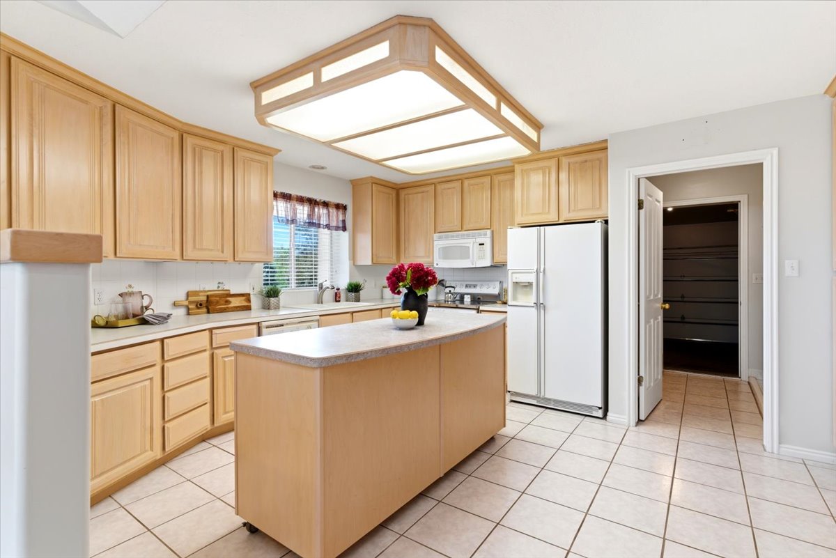 Kitchen featuring light wood cabinetry, white countertops, a moveable center island with a light-toned surface, tile flooring, and a pantry with built-in shelving