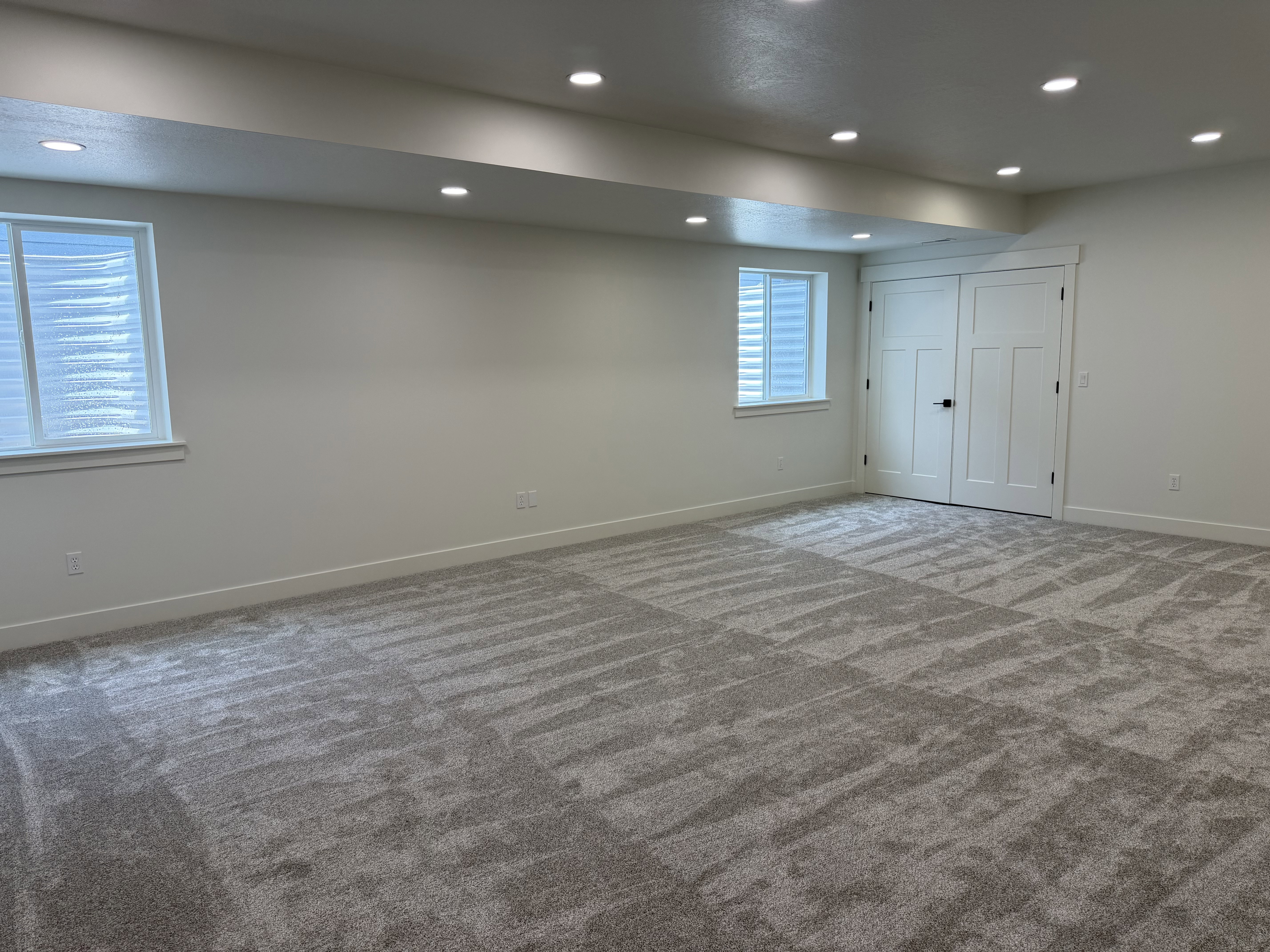 Spacious room featuring new patterned carpet, recessed lighting, two windows with blinds, and white double doors
