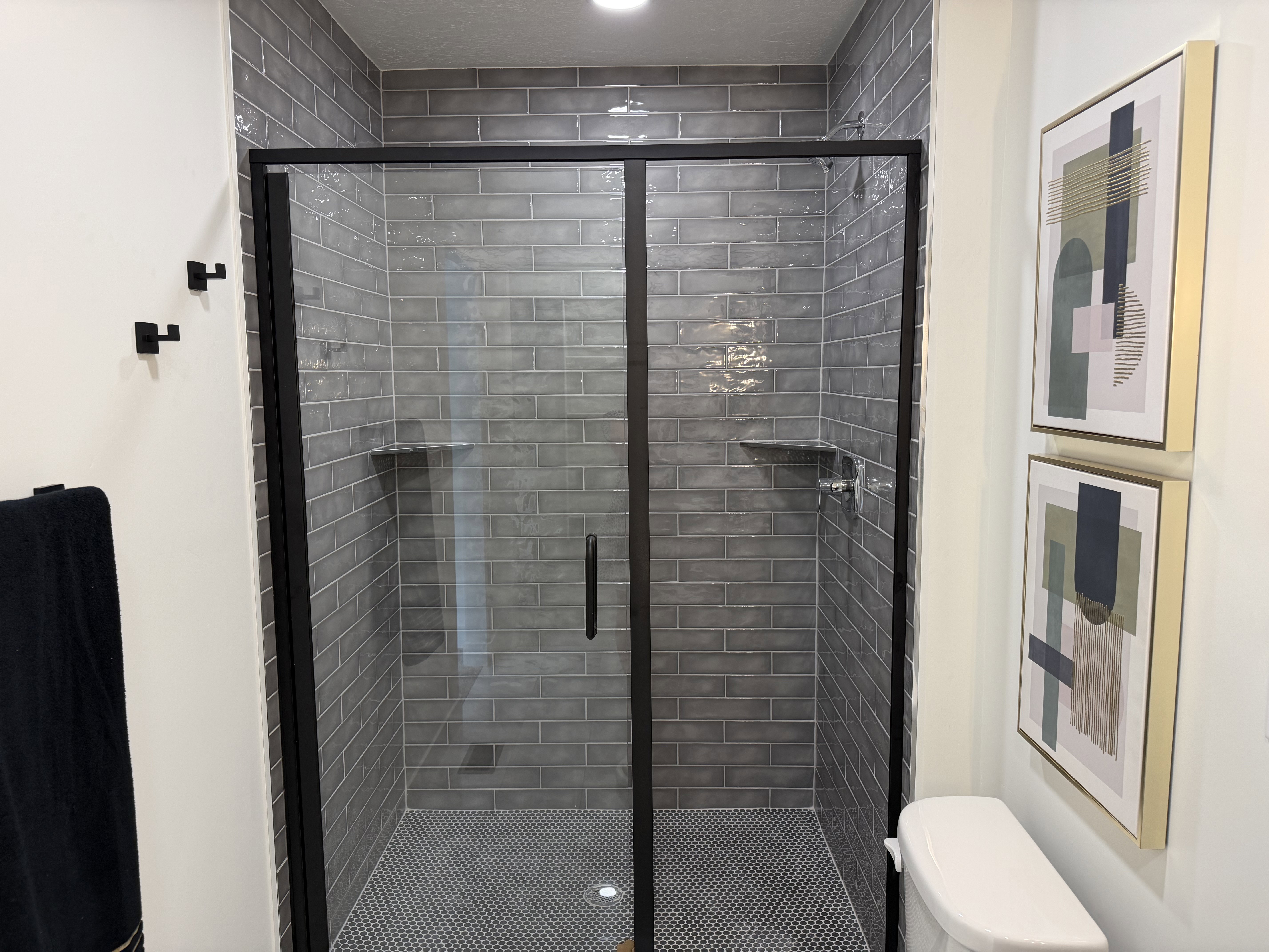 Shower enclosure featuring black-framed glass doors, grey subway tile surround, and built-in shelving