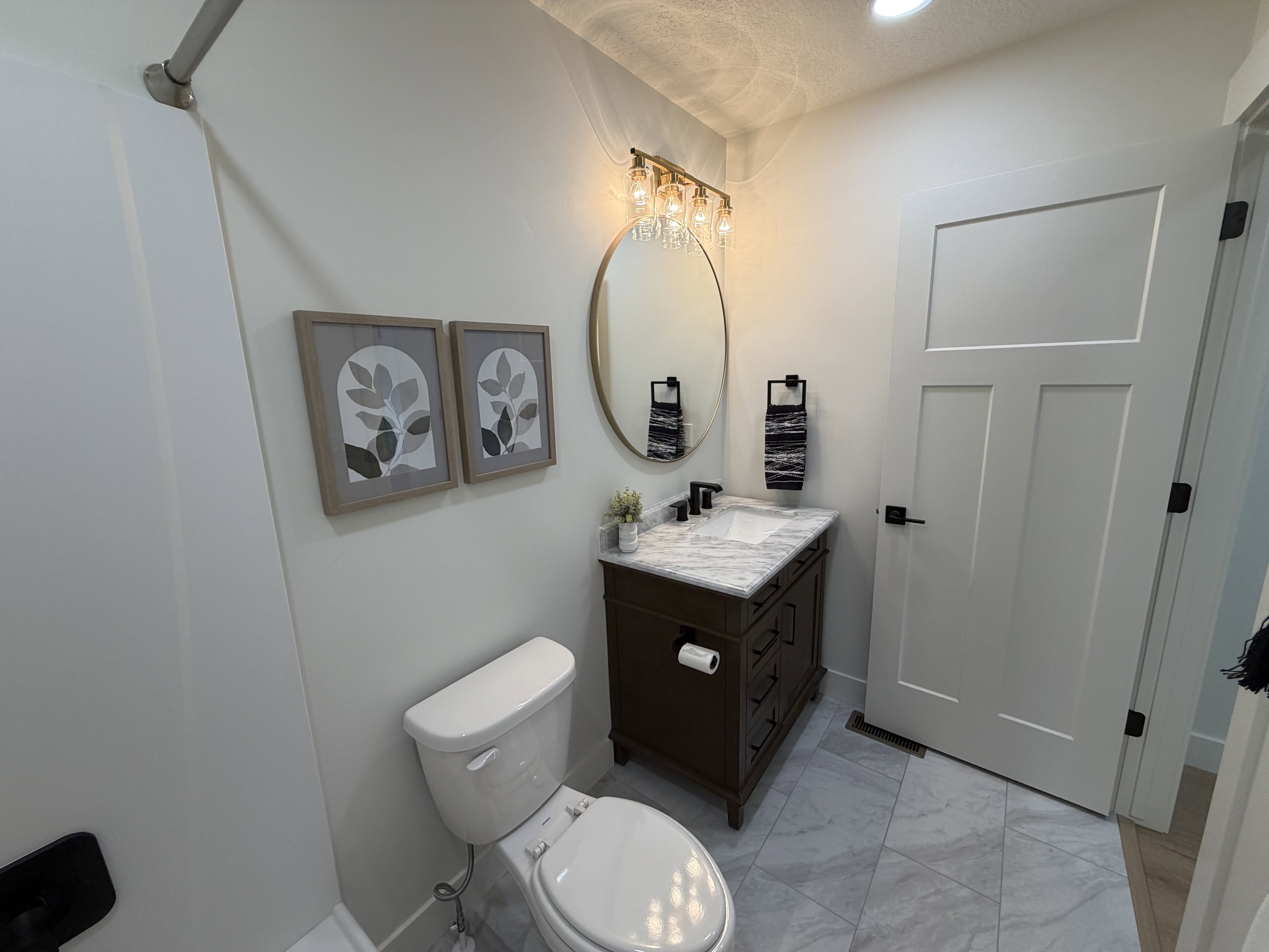 Bathroom featuring a dark wood vanity with a white marble countertop and integrated sink, matte black faucet, and oval gold-framed mirror