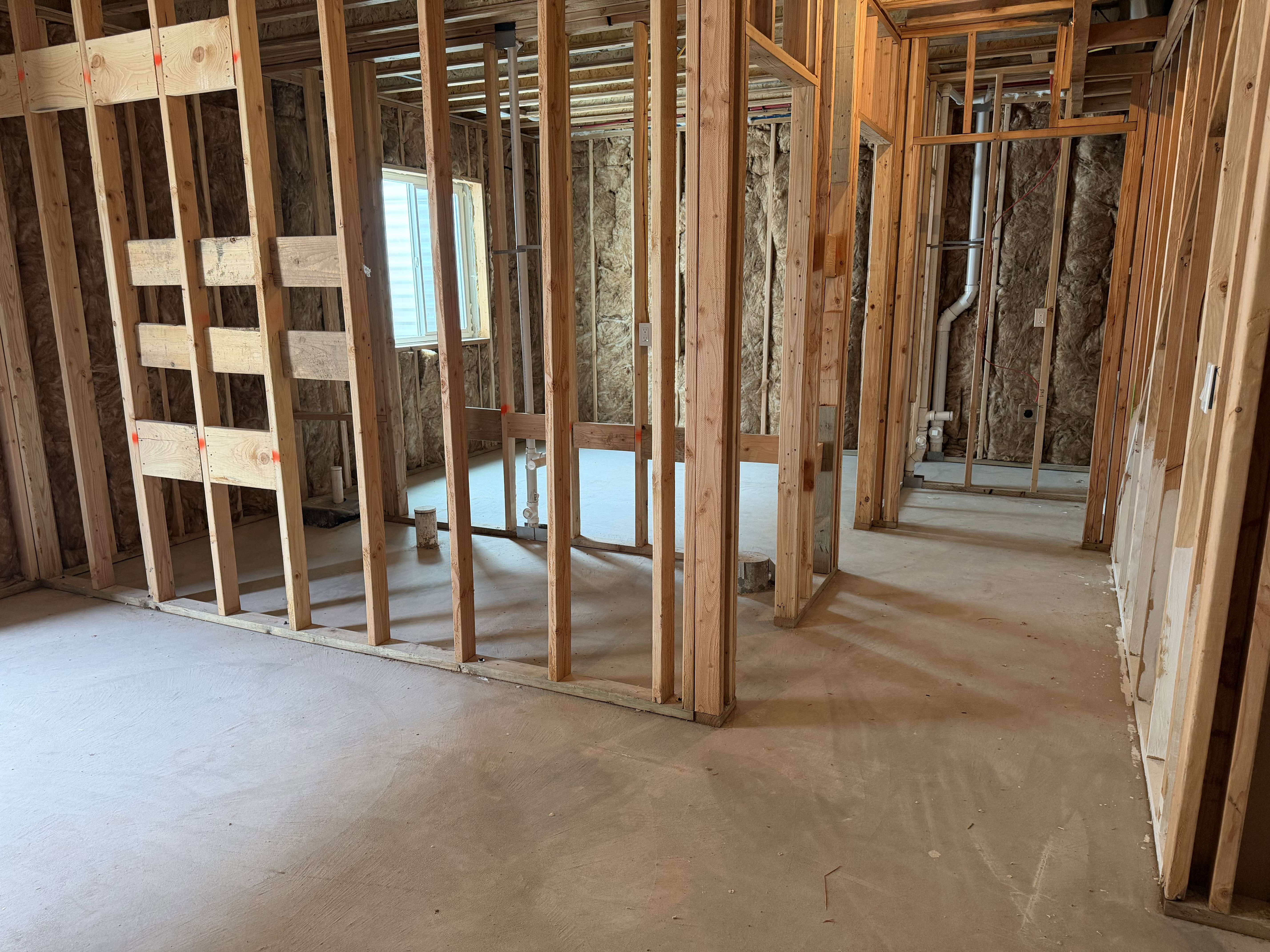 Unfinished interior space featuring wood framing, exposed insulation, a single window, and concrete flooring