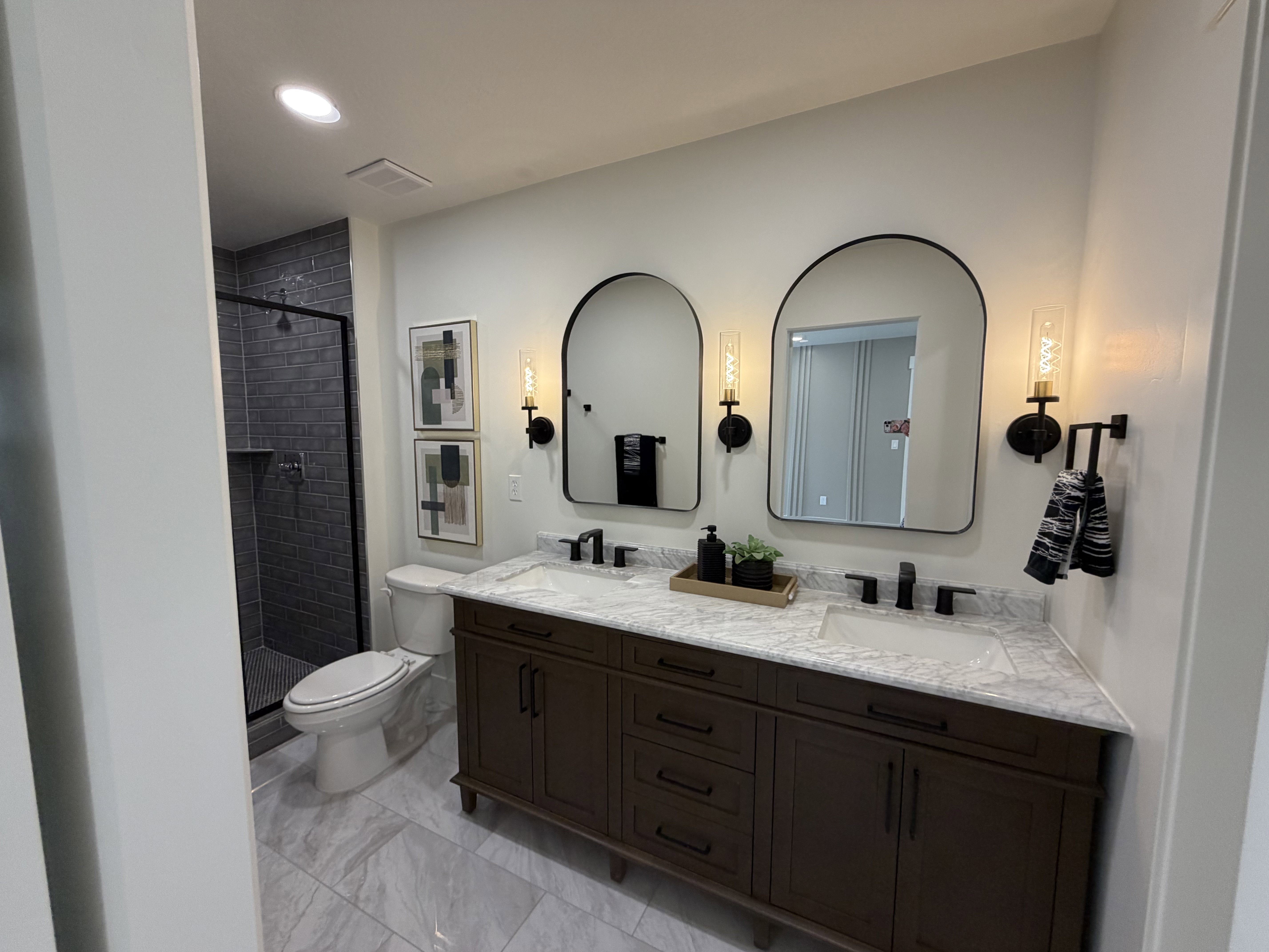 Bathroom featuring a dual vanity with a stone-finish countertop, dark wood-finish cabinetry, and matte black fixtures