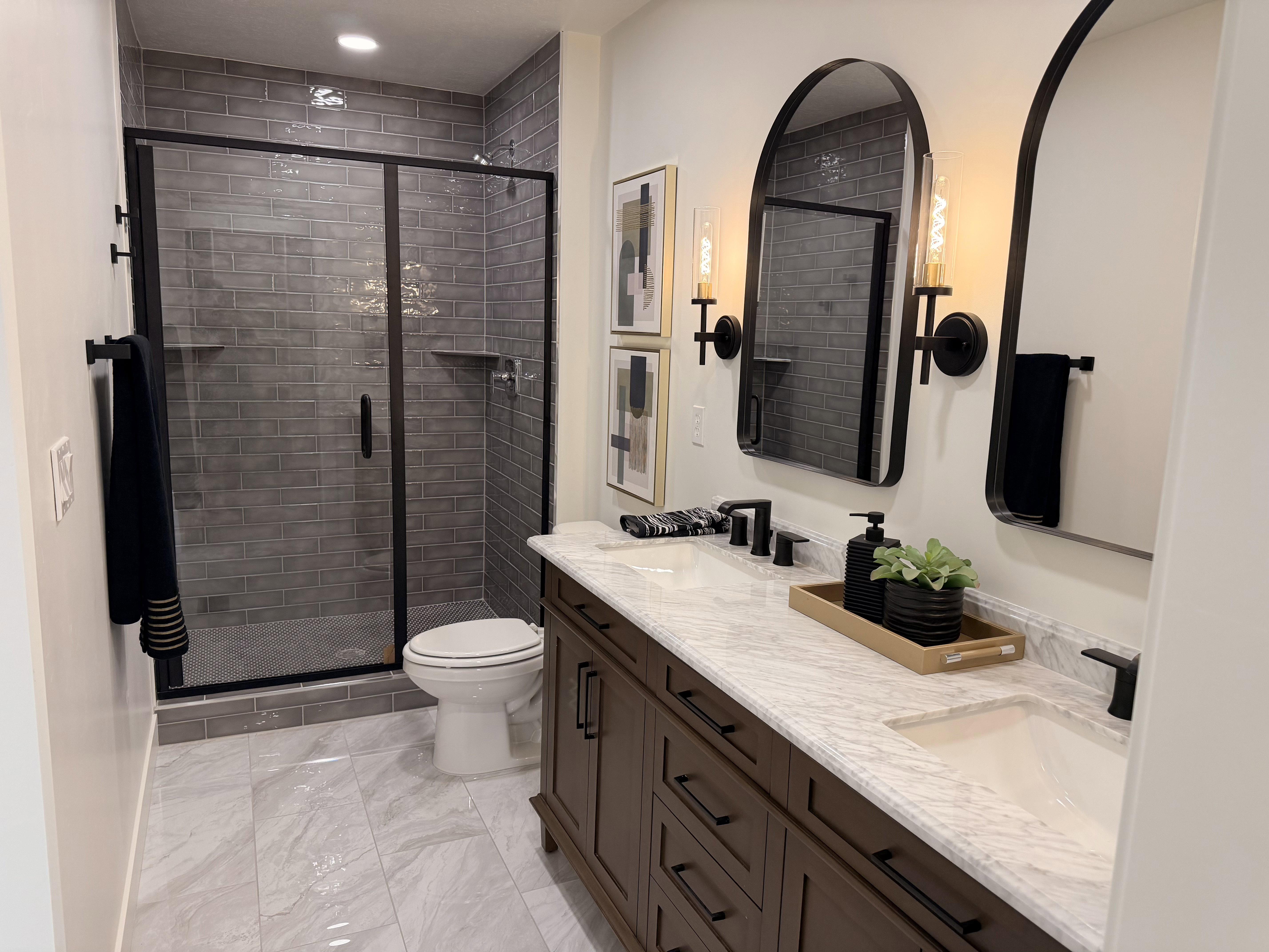 Bathroom featuring a dual vanity with a light-toned countertop, dark wood-finish cabinetry, and black fixtures