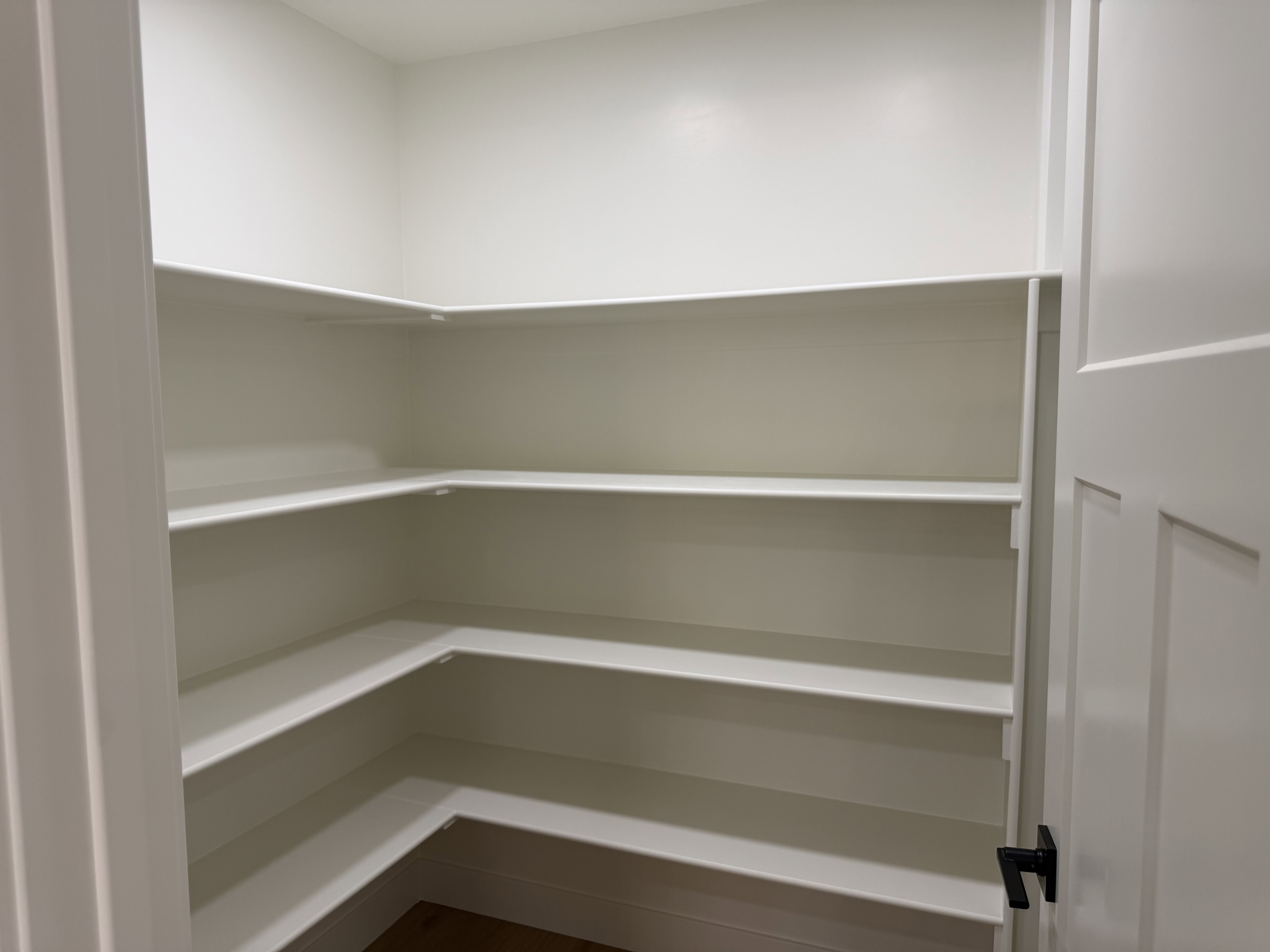 Spacious corner pantry featuring multiple levels of shelving, a white interior finish, and a solid-core door with matte black hardware