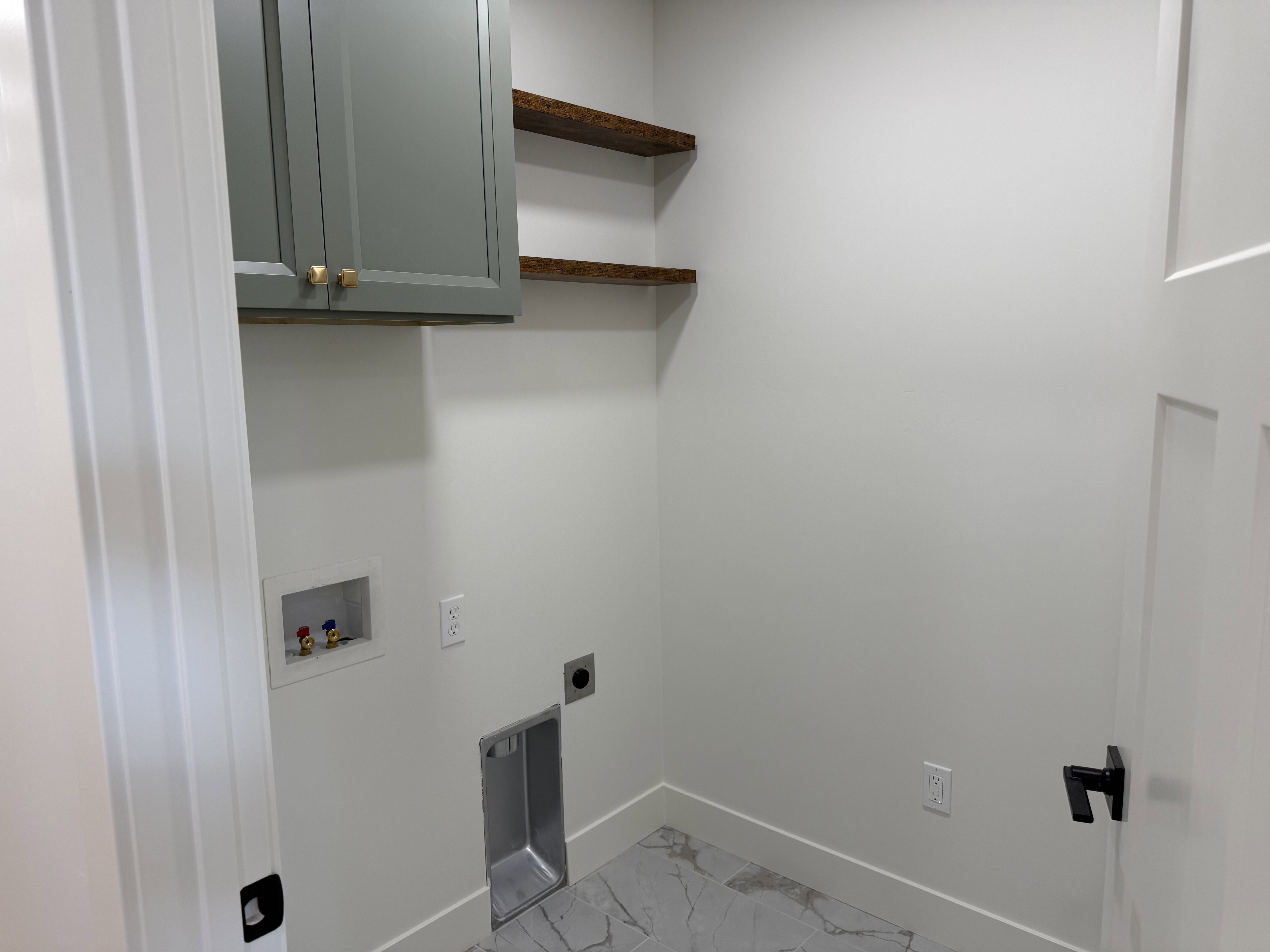Laundry room featuring a light gray wall cabinet with gold hardware, two rustic wood floating shelves, a utility sink, and light gray marble-look flooring