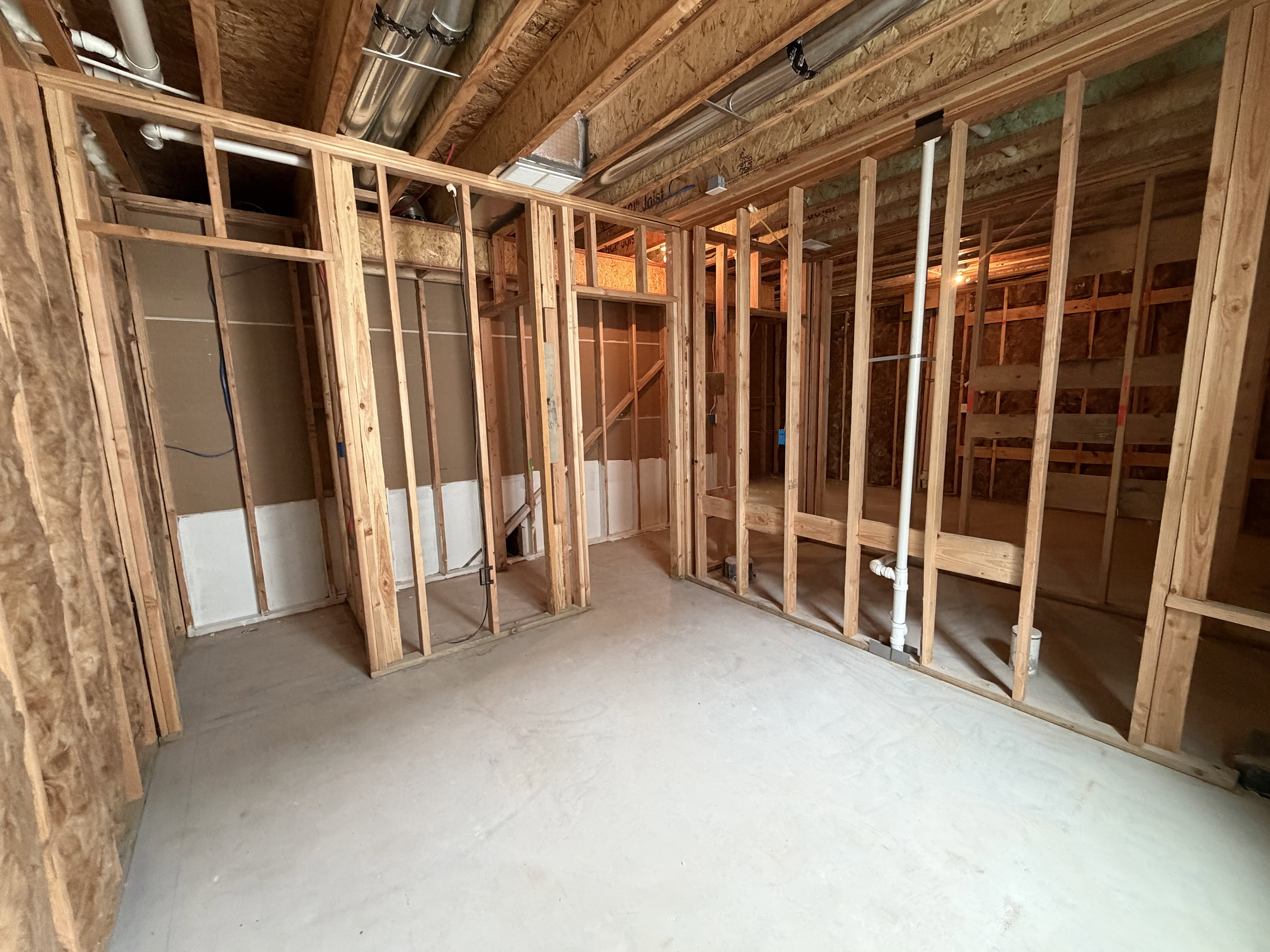 Unfinished basement featuring exposed wood framing, concrete flooring, visible overhead ductwork, and plumbing rough-ins