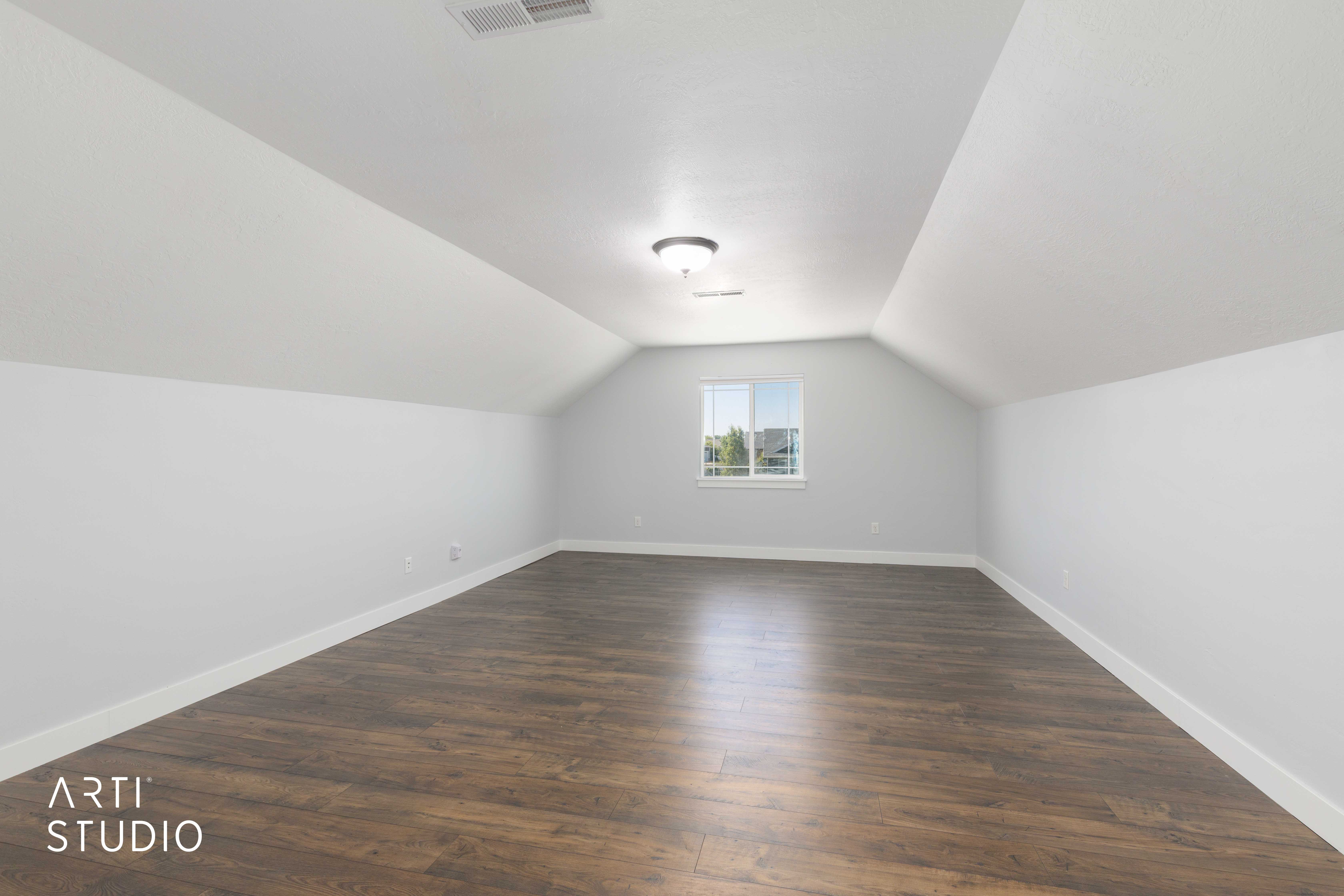 Spacious bonus room featuring wood-finish flooring, a window providing natural light, a ceiling-mounted light fixture, and white baseboards