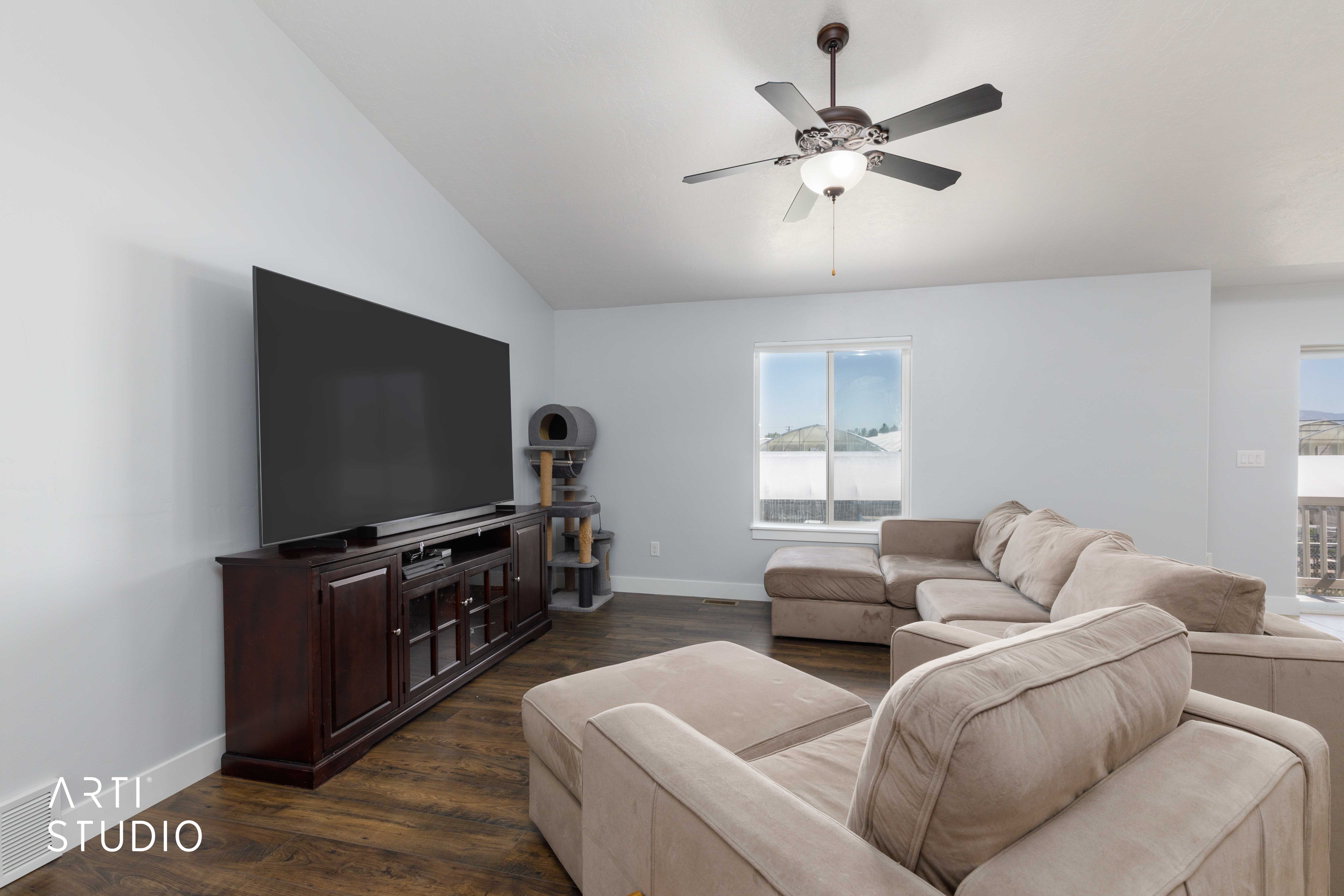 Spacious living area featuring light-toned walls, wood-finish flooring, and a ceiling fan with integrated lighting