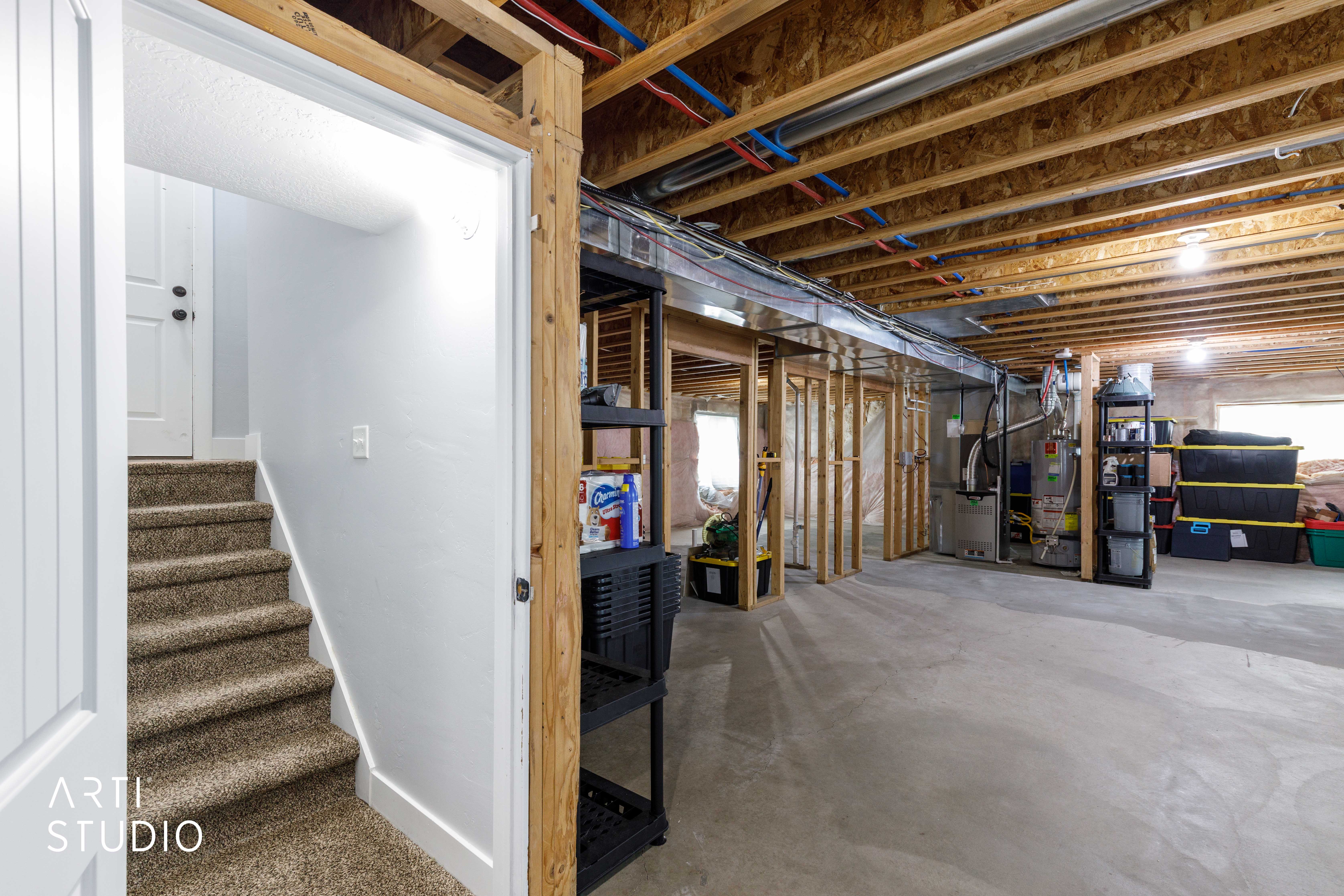 Stairwell entry leading to an unfinished basement featuring concrete flooring, exposed ceiling joists, and framed partition walls