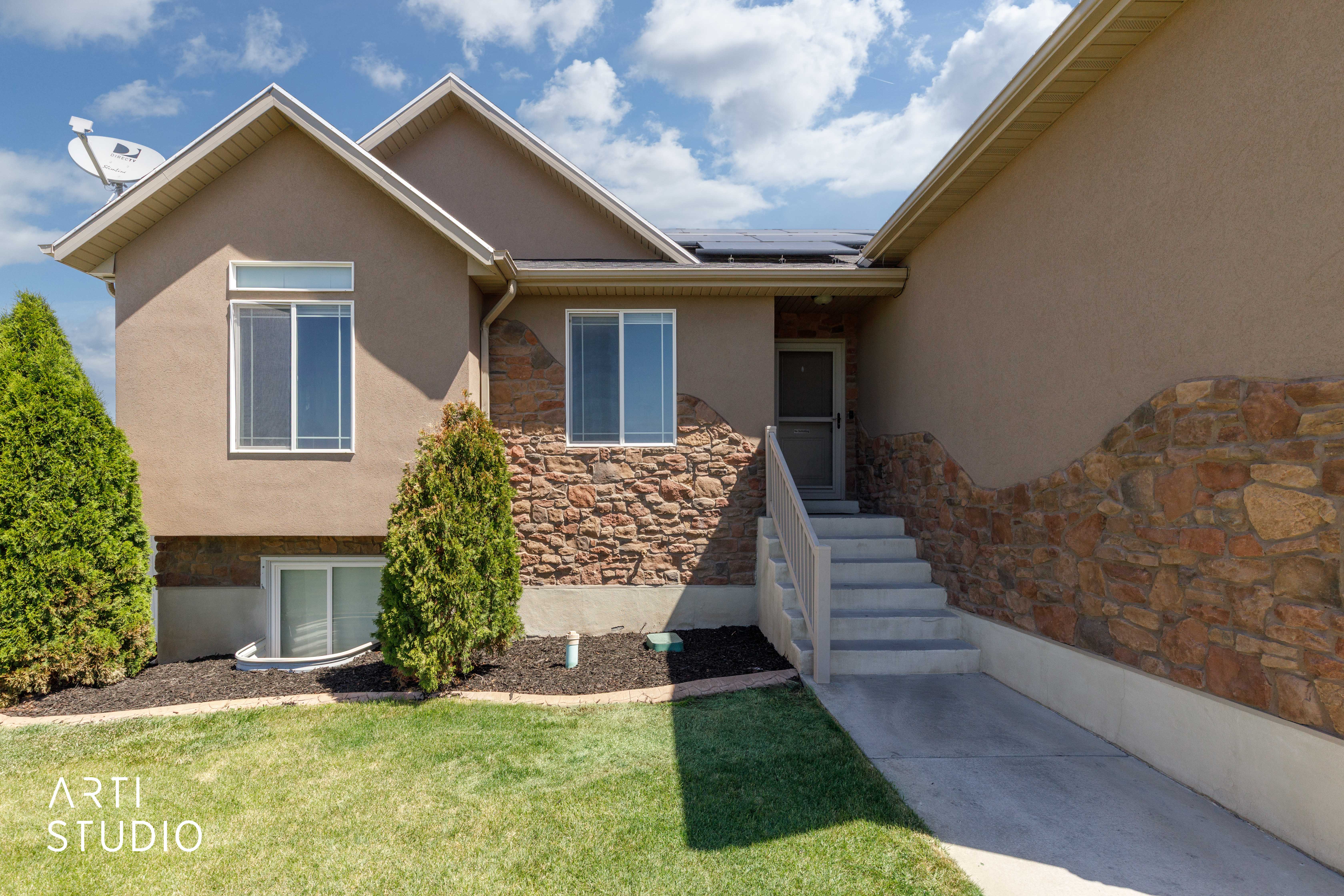 Stucco and stone facade with multiple windows, concrete steps, and integrated solar panels