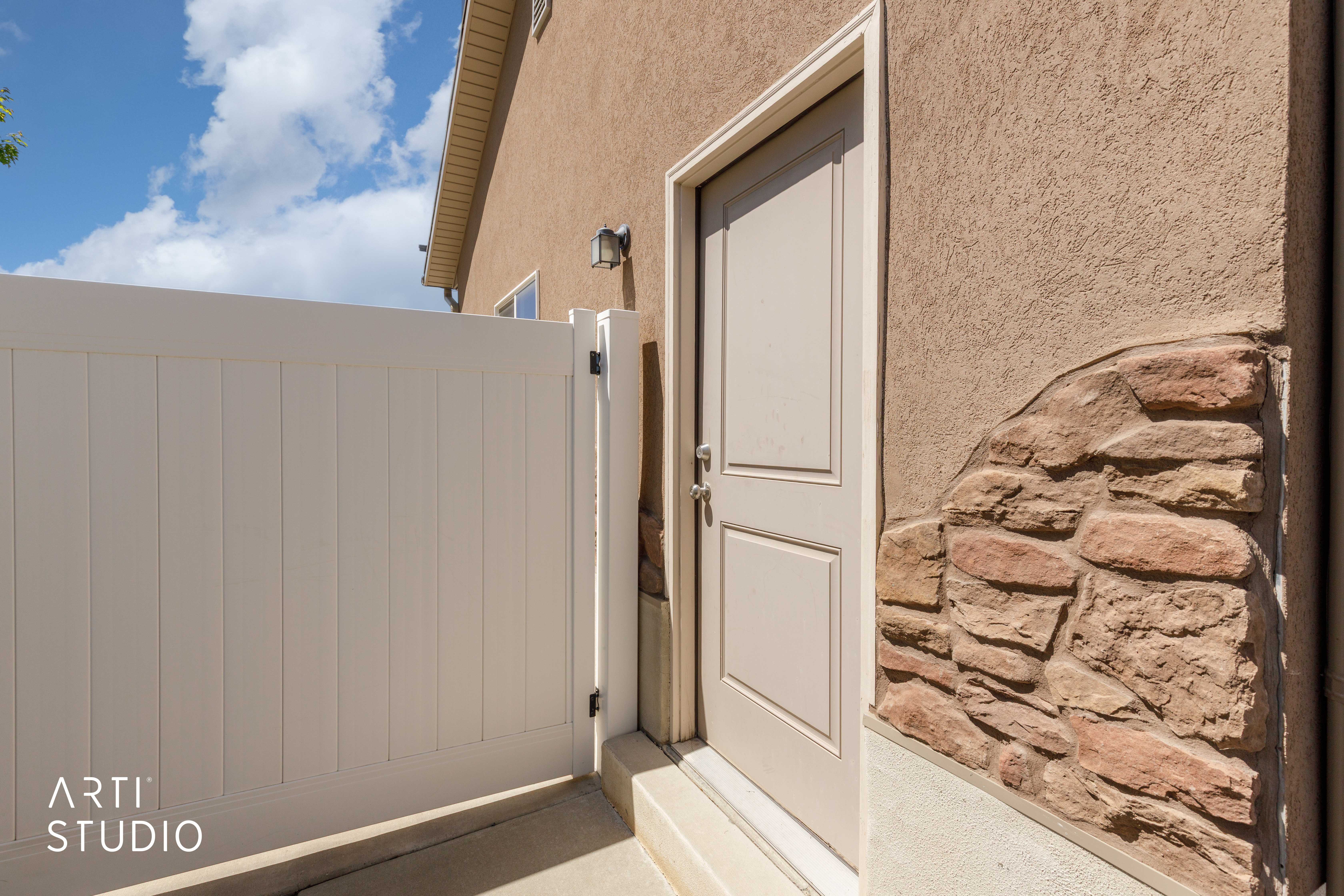 Exterior entryway featuring a white paneled door, decorative stone accents, stucco siding, and an outdoor wall sconce