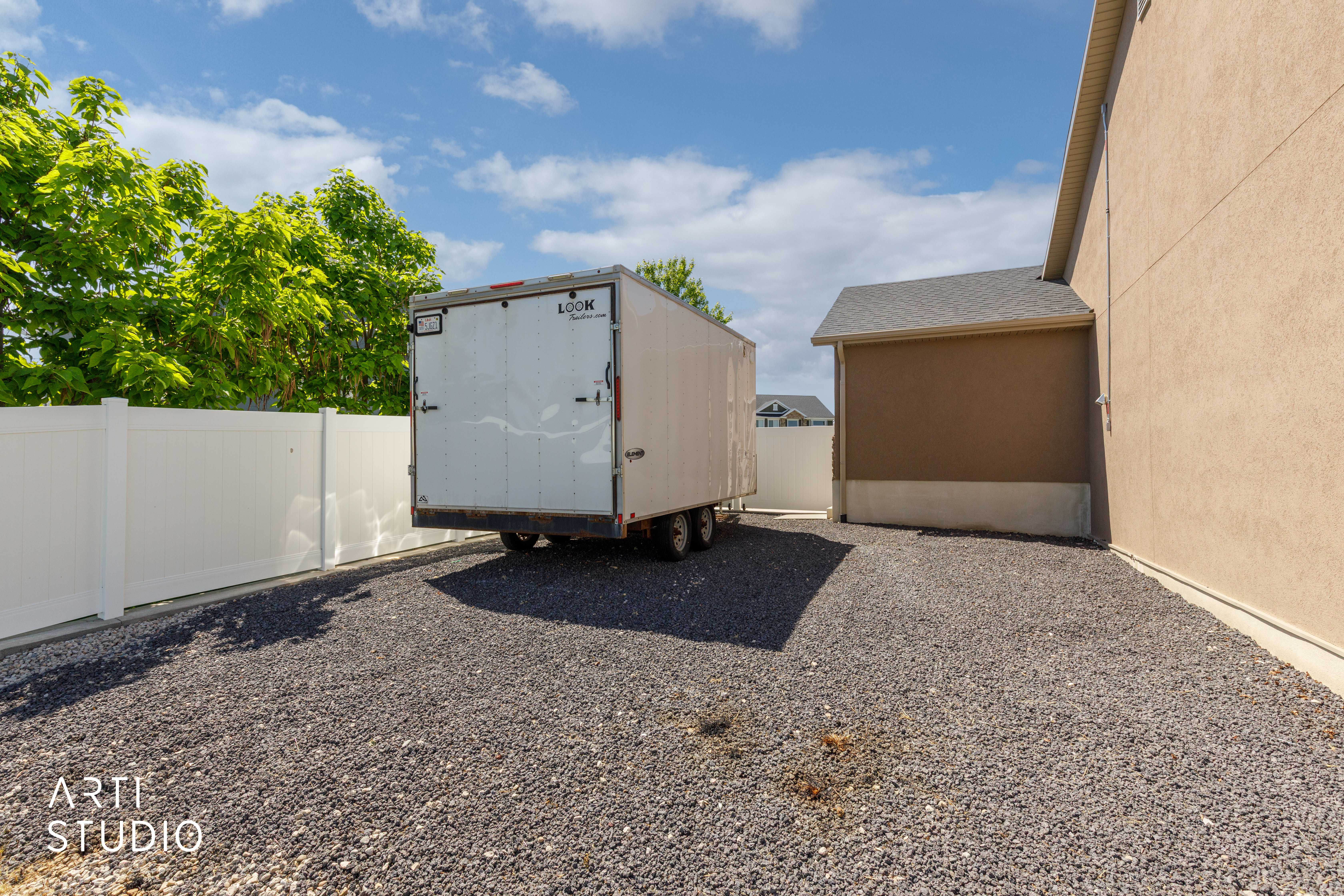Gravel parking area featuring a white vinyl fence and stucco exterior