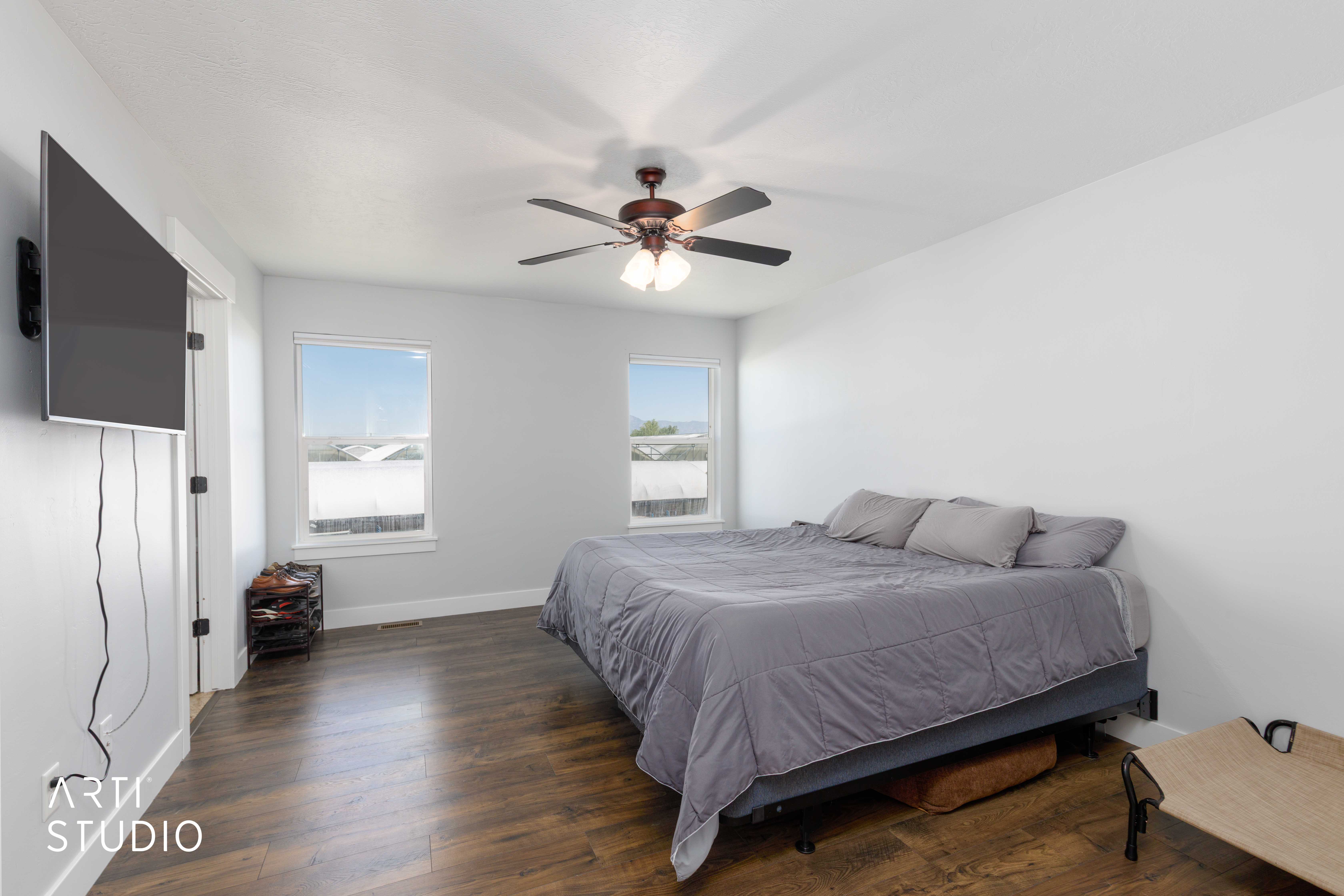 Spacious bedroom featuring wood-finish flooring, two windows with white trim, and a ceiling fan with integrated lighting