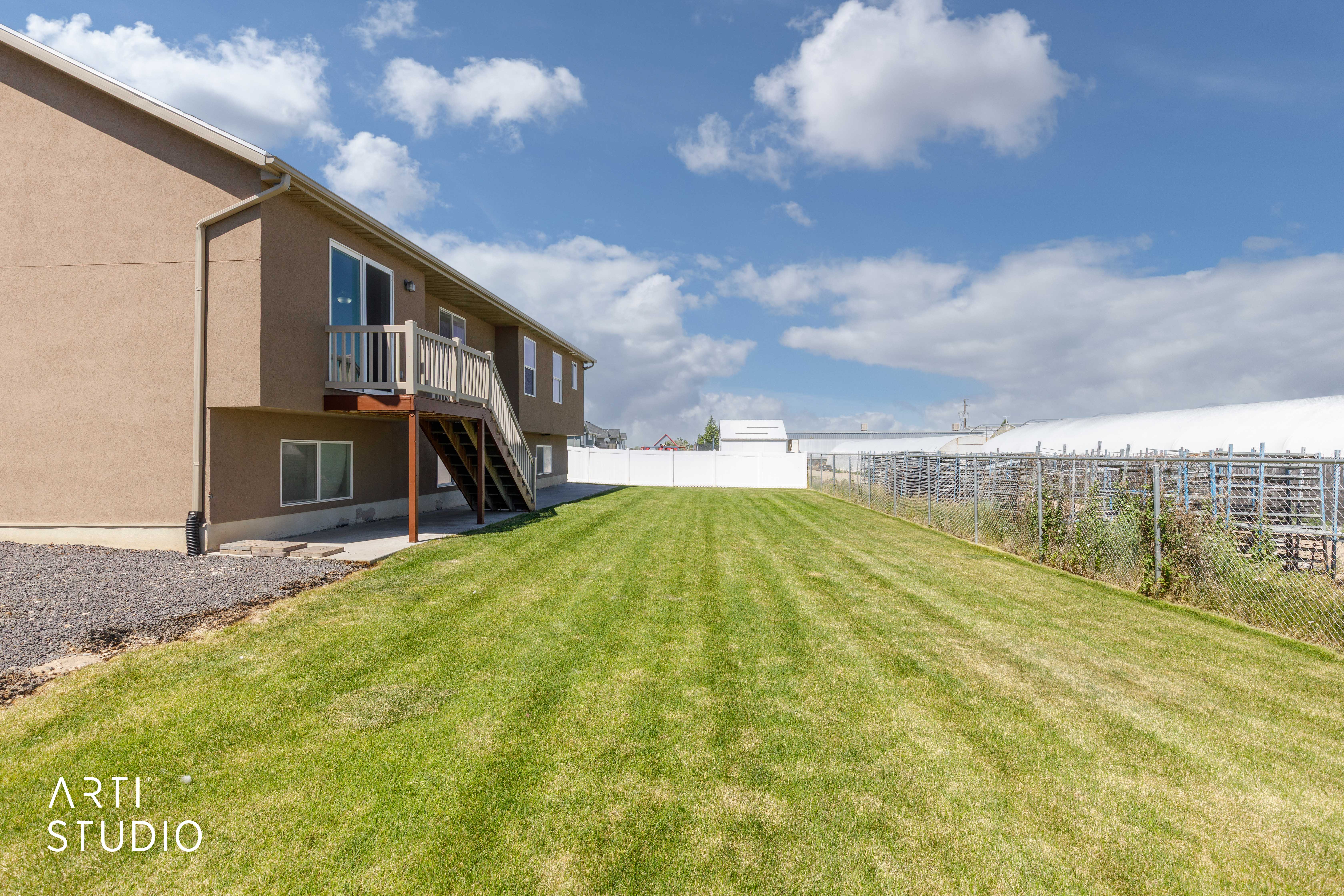 Expansive backyard featuring a large green lawn, brown stucco exterior, a two-story deck with white railings, and a white privacy fence