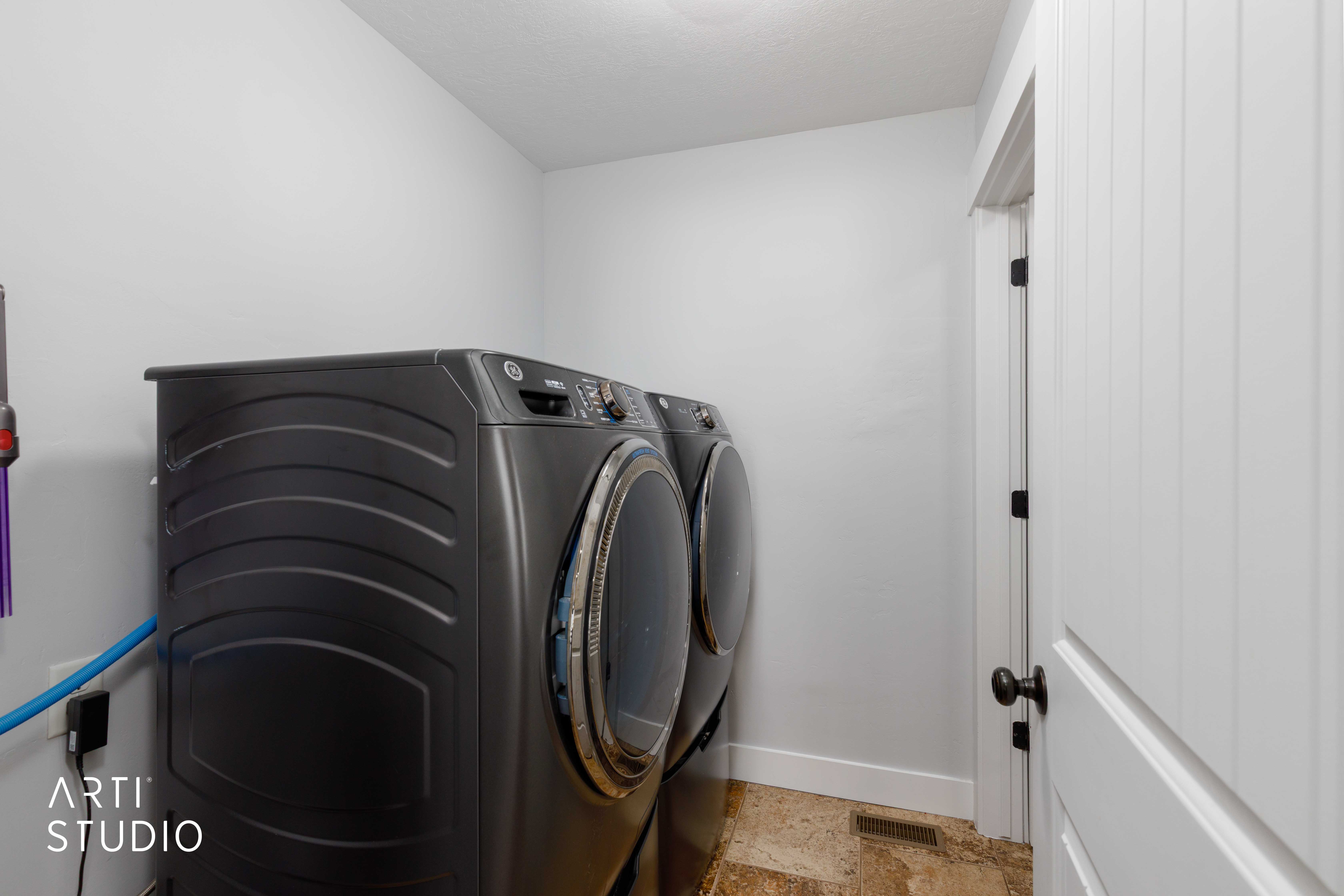 Dedicated laundry space featuring a white paneled door with matte black hardware, light-toned wall paint, and wood-finish flooring