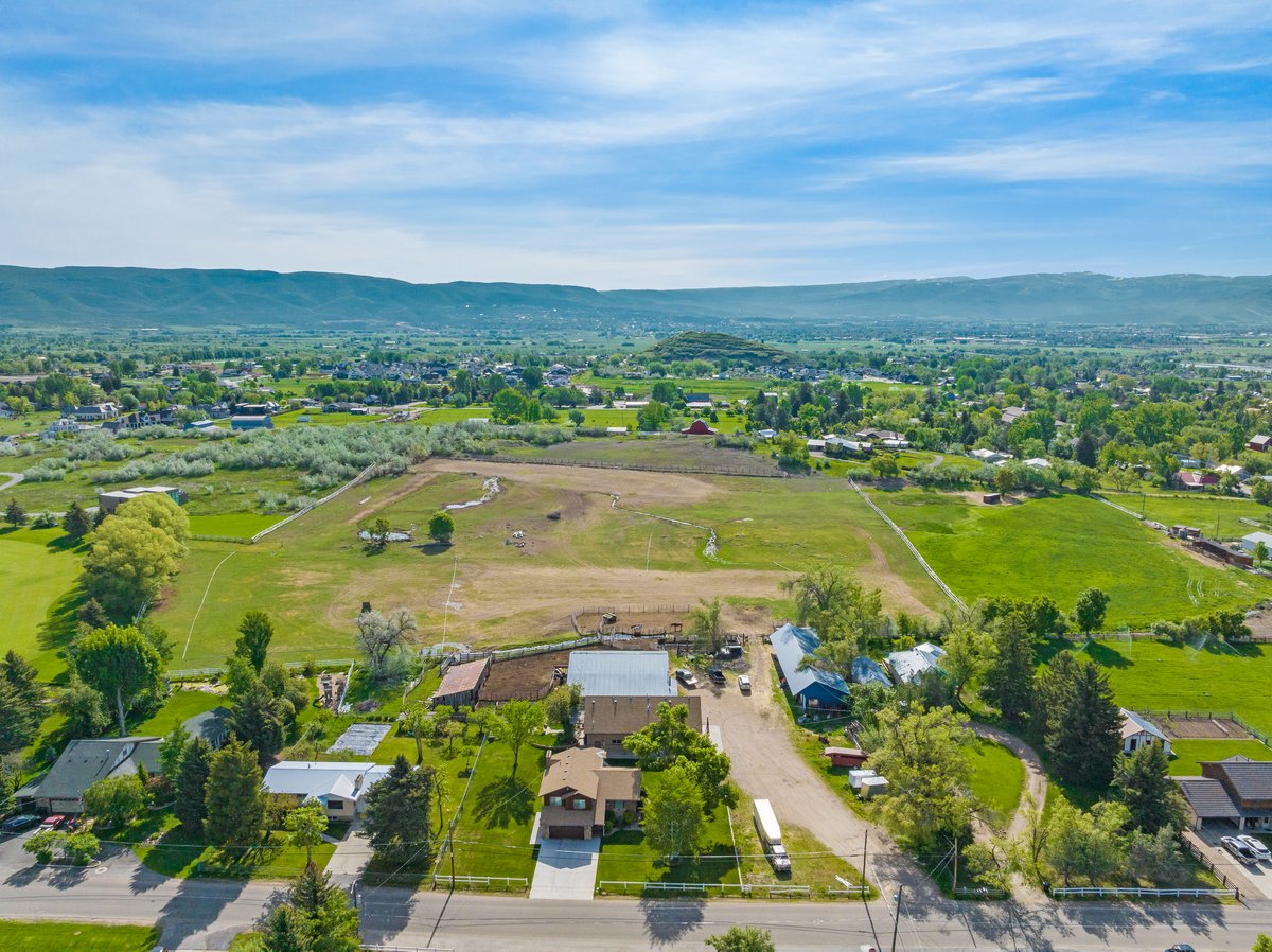 Aerial perspective showcasing the property's expansive green lawn and mature trees, surrounded by a rural landscape with agricultural fields and distant mountainous terrain