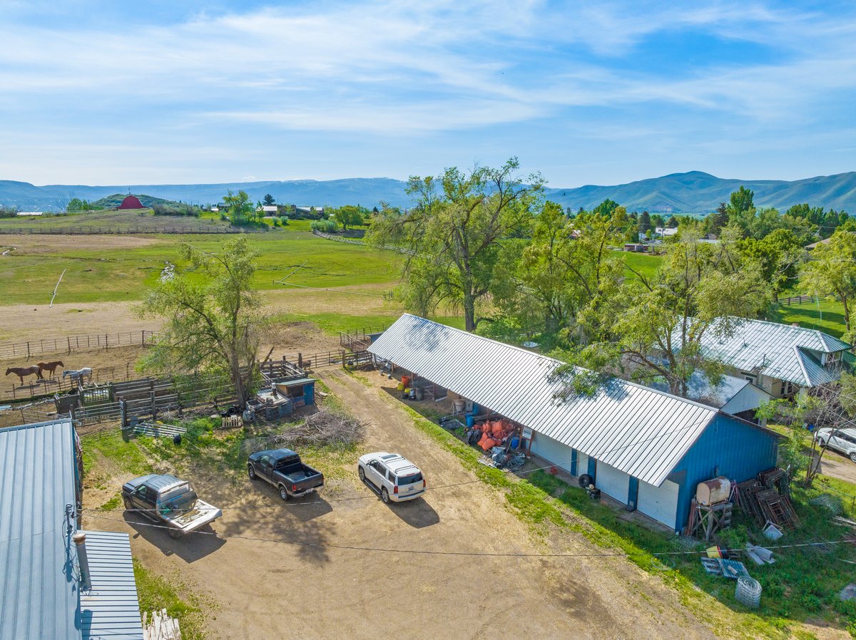Expansive rural property featuring multiple outbuildings with metal roofs, fenced paddock areas, and abundant mature trees