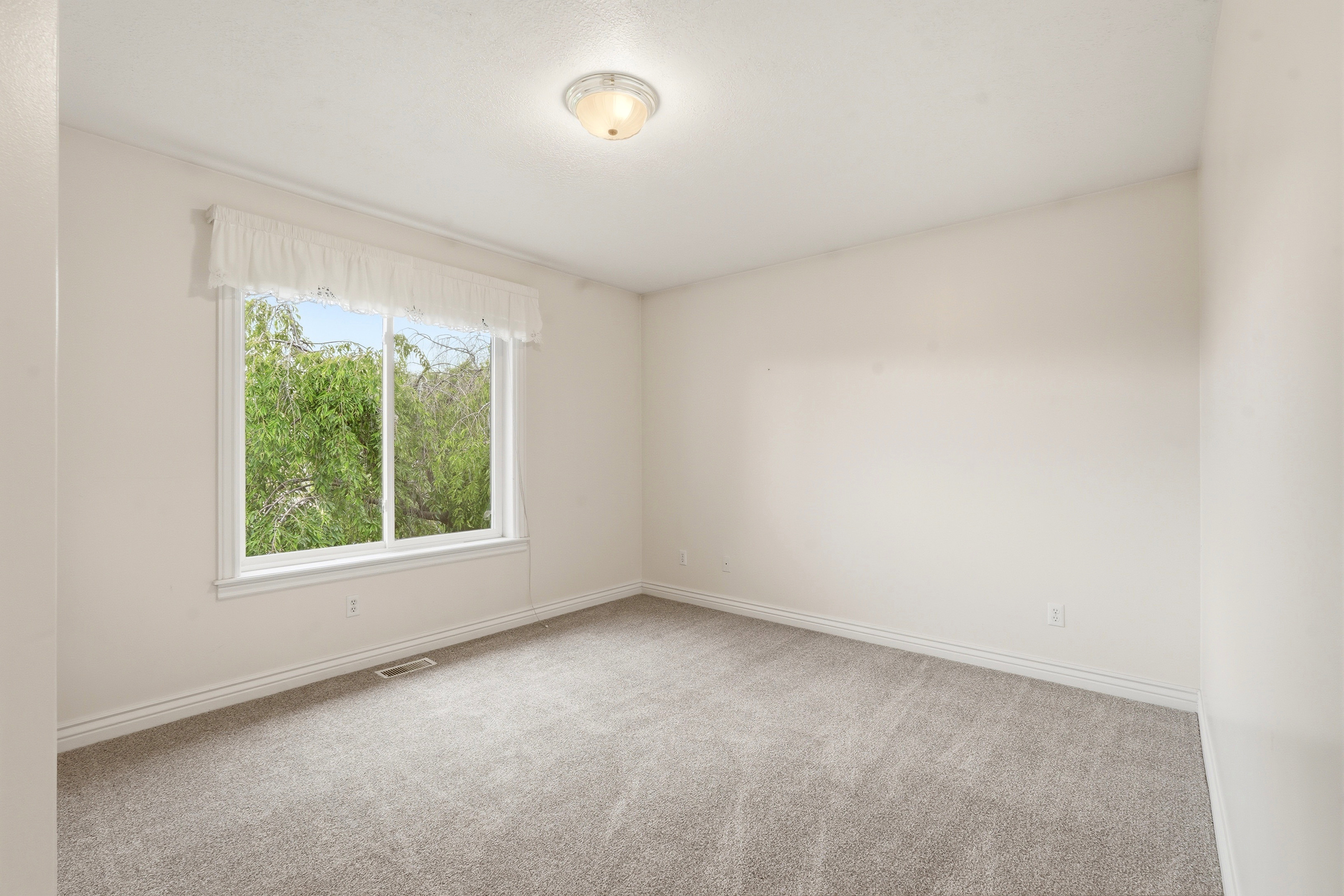 Bright room featuring a large window, neutral carpeting, white baseboards, and a semi-flush mount ceiling light fixture