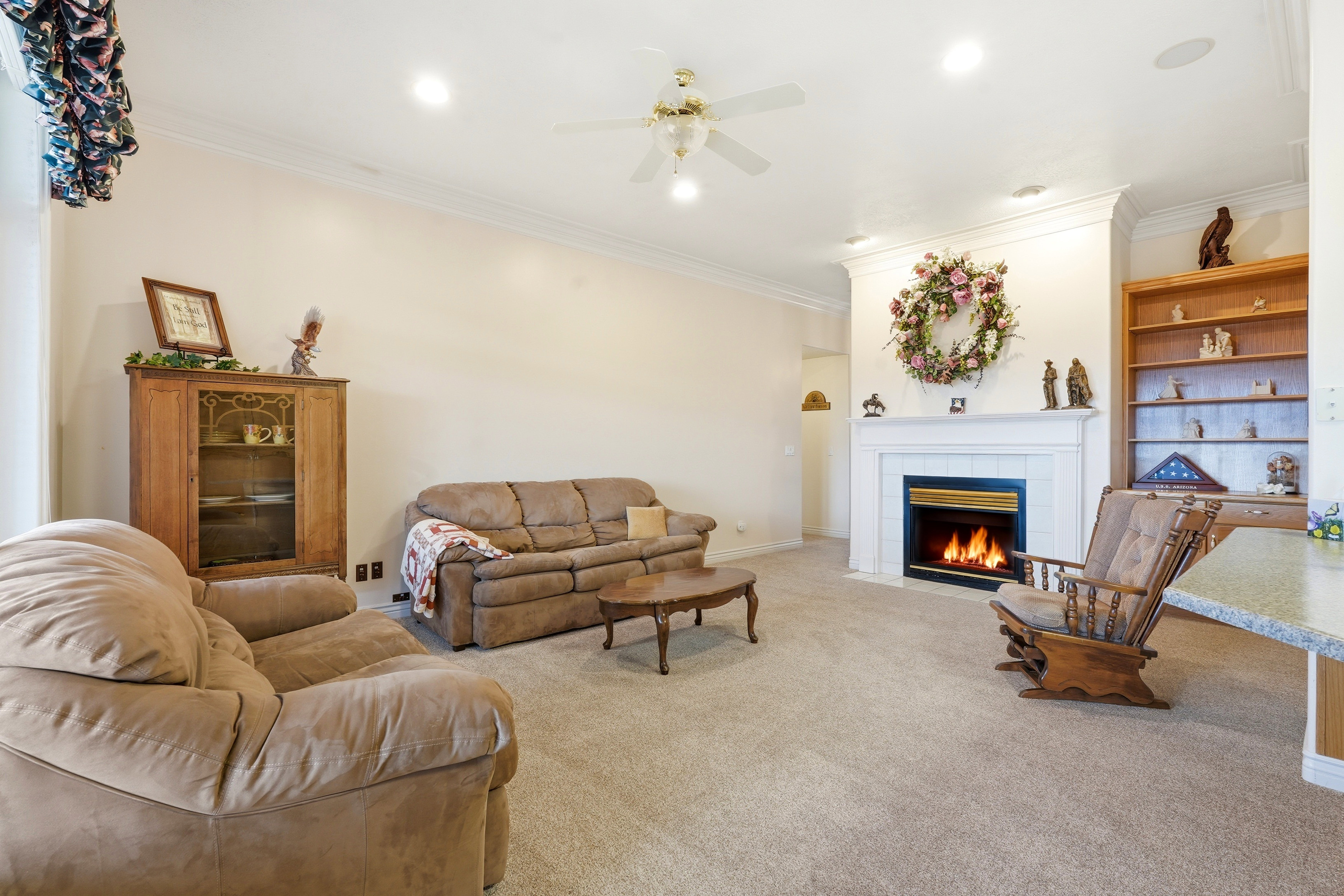 Living area featuring a fireplace with a white mantel, recessed lighting, crown molding, a ceiling fan, and built-in shelving