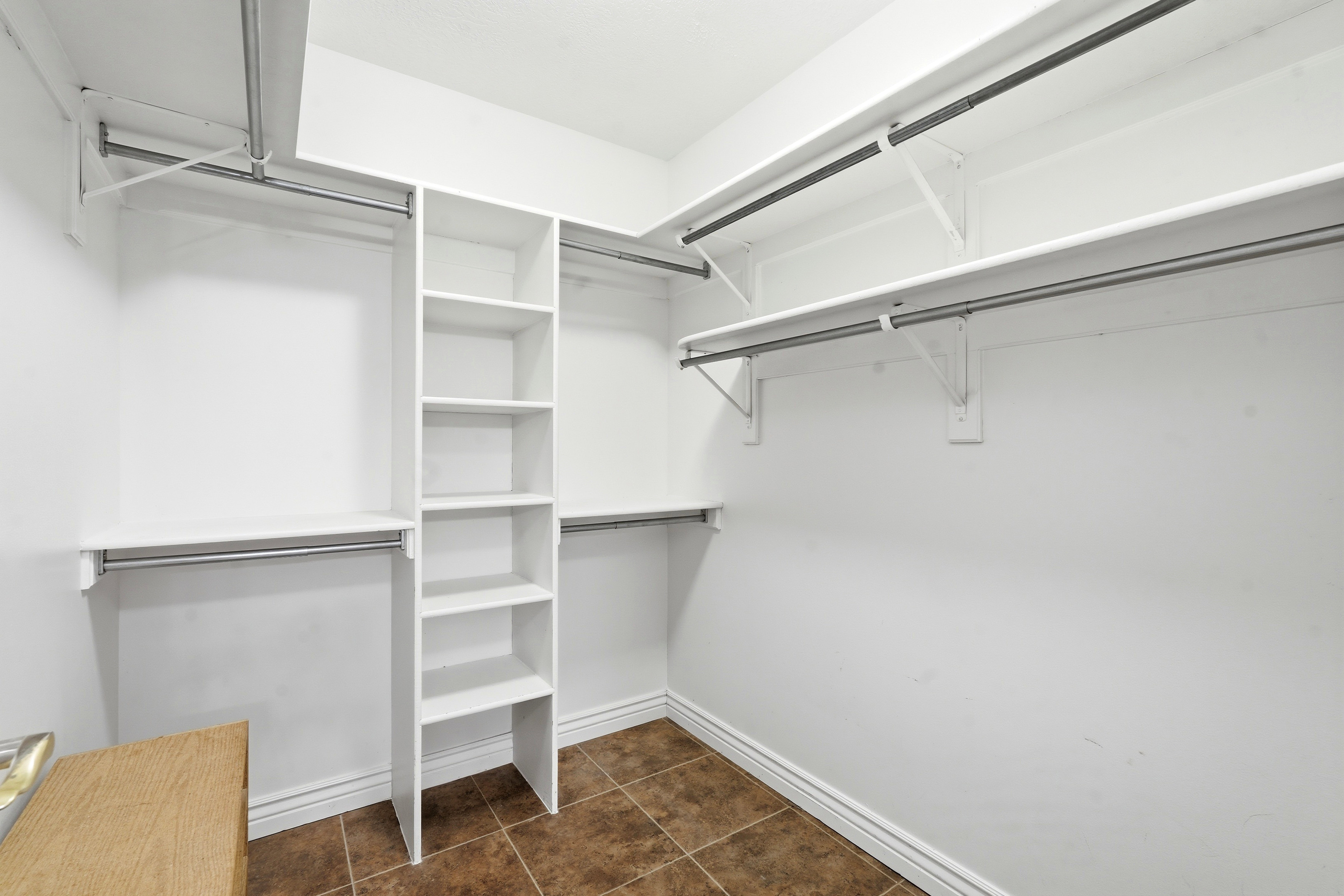 Walk-in closet featuring built-in shelving, multiple hanging rods, white walls, white baseboards, and a tile floor