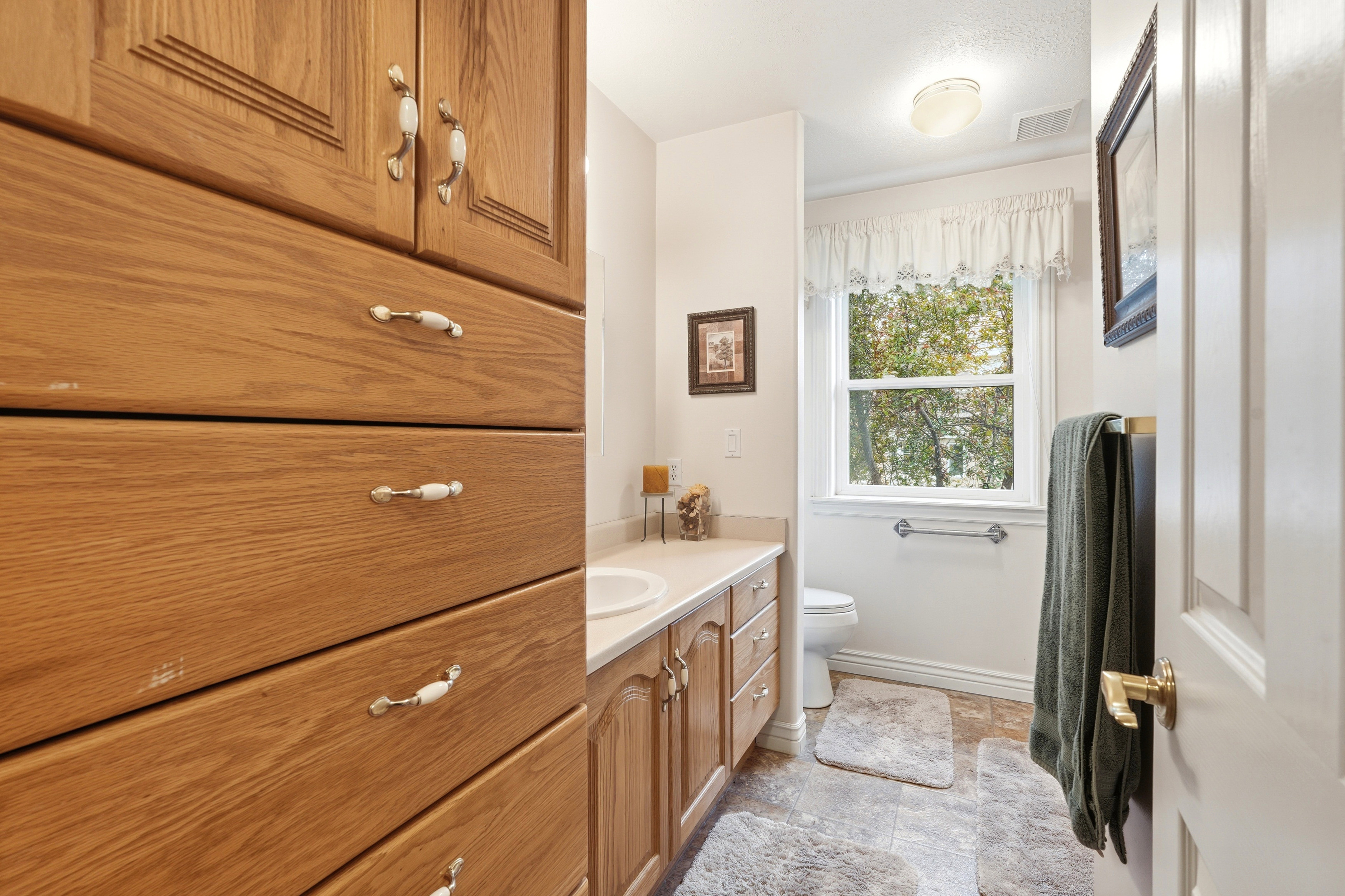 Bathroom featuring extensive wood-finish cabinetry, a window with a valance, tile flooring, and a vanity with an integrated sink