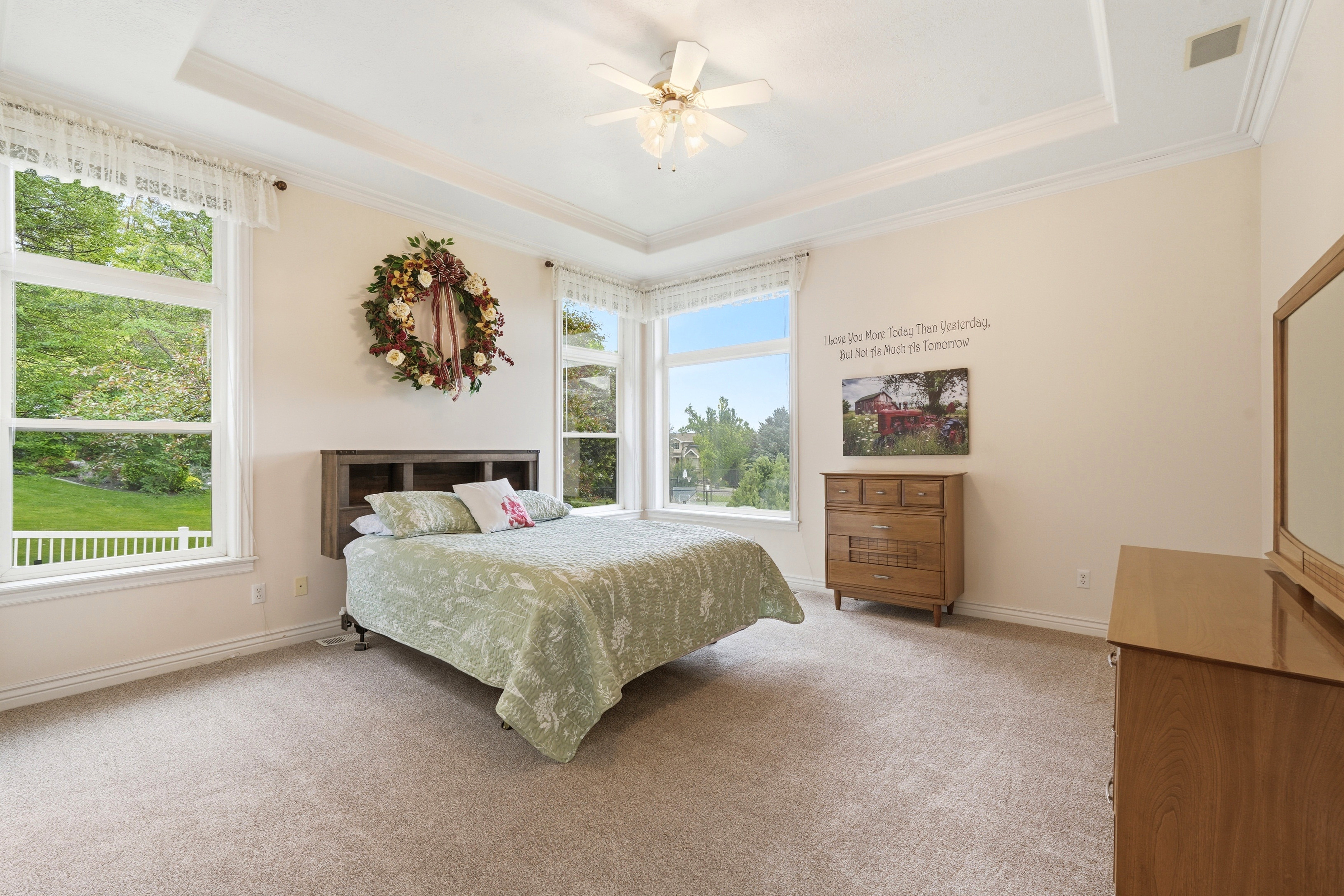 Spacious room featuring tray ceiling, ceiling fan with integrated lighting, multiple large windows, and neutral carpet flooring
