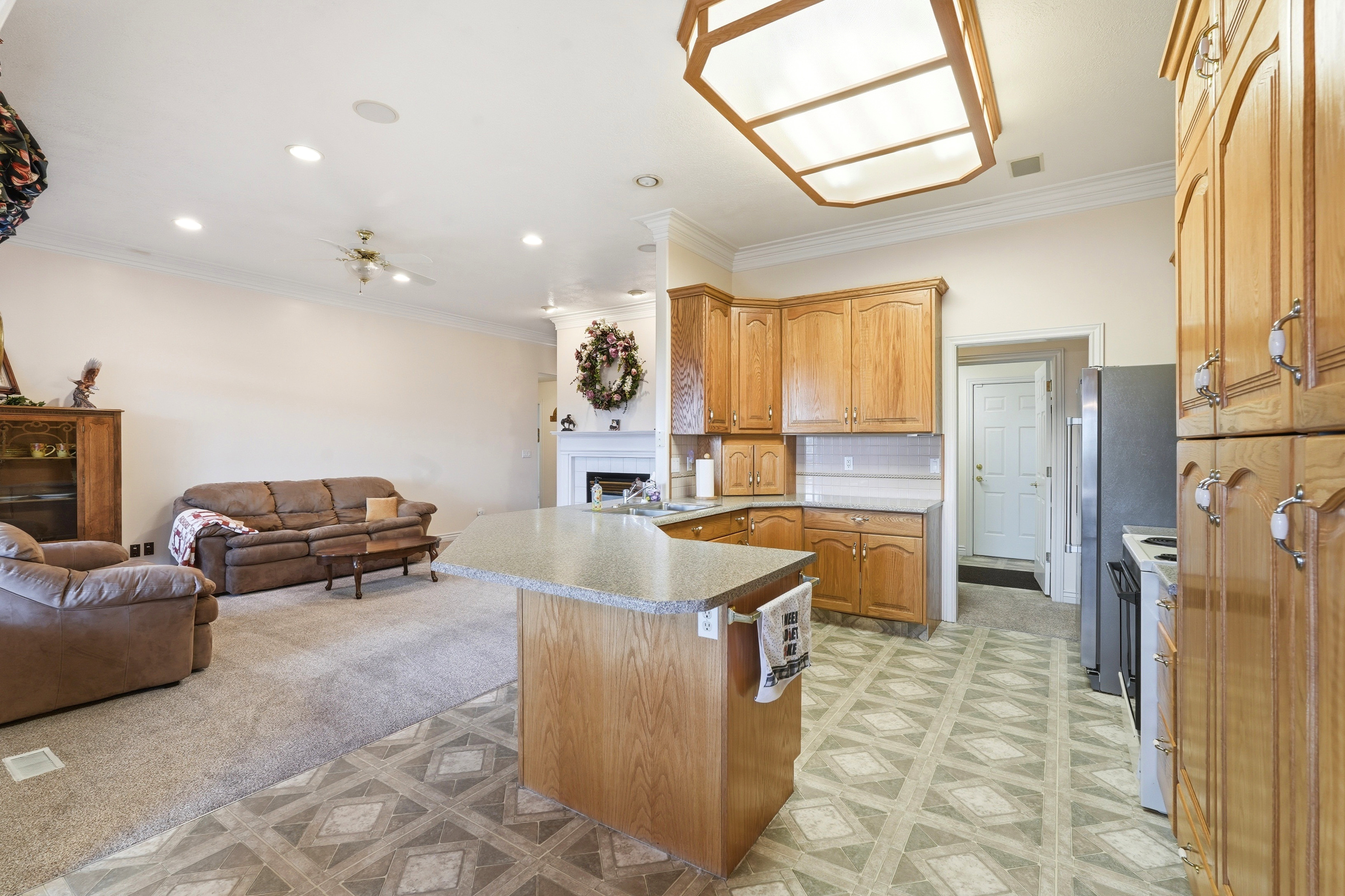 Open-concept kitchen and living area featuring wood-finish cabinetry, a central island with countertop seating, geometric pattern flooring, a fireplace with a mantel, and recessed lighting