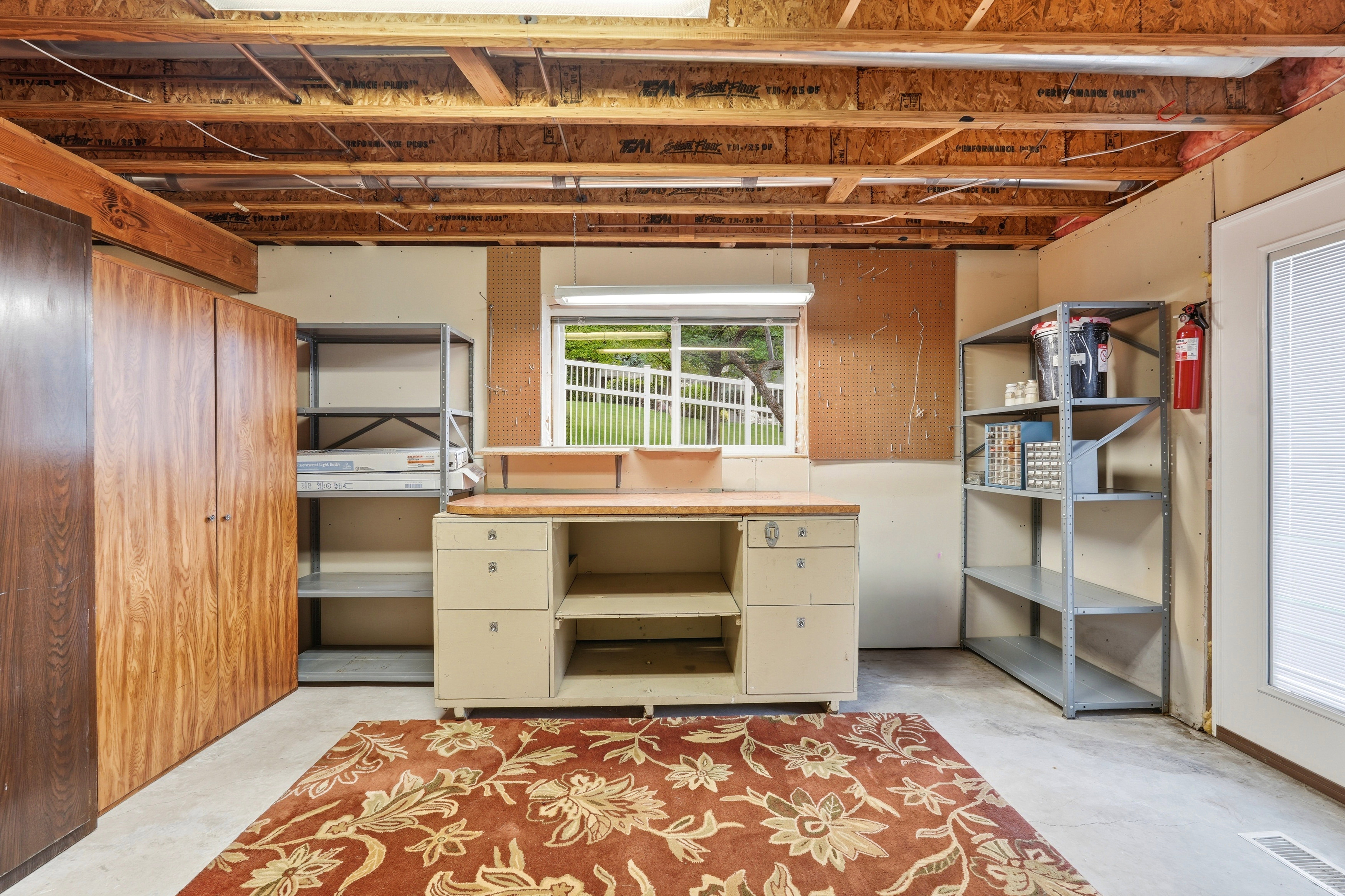 Lower-level utility space featuring exposed ceiling joists, a built-in workbench, and concrete flooring