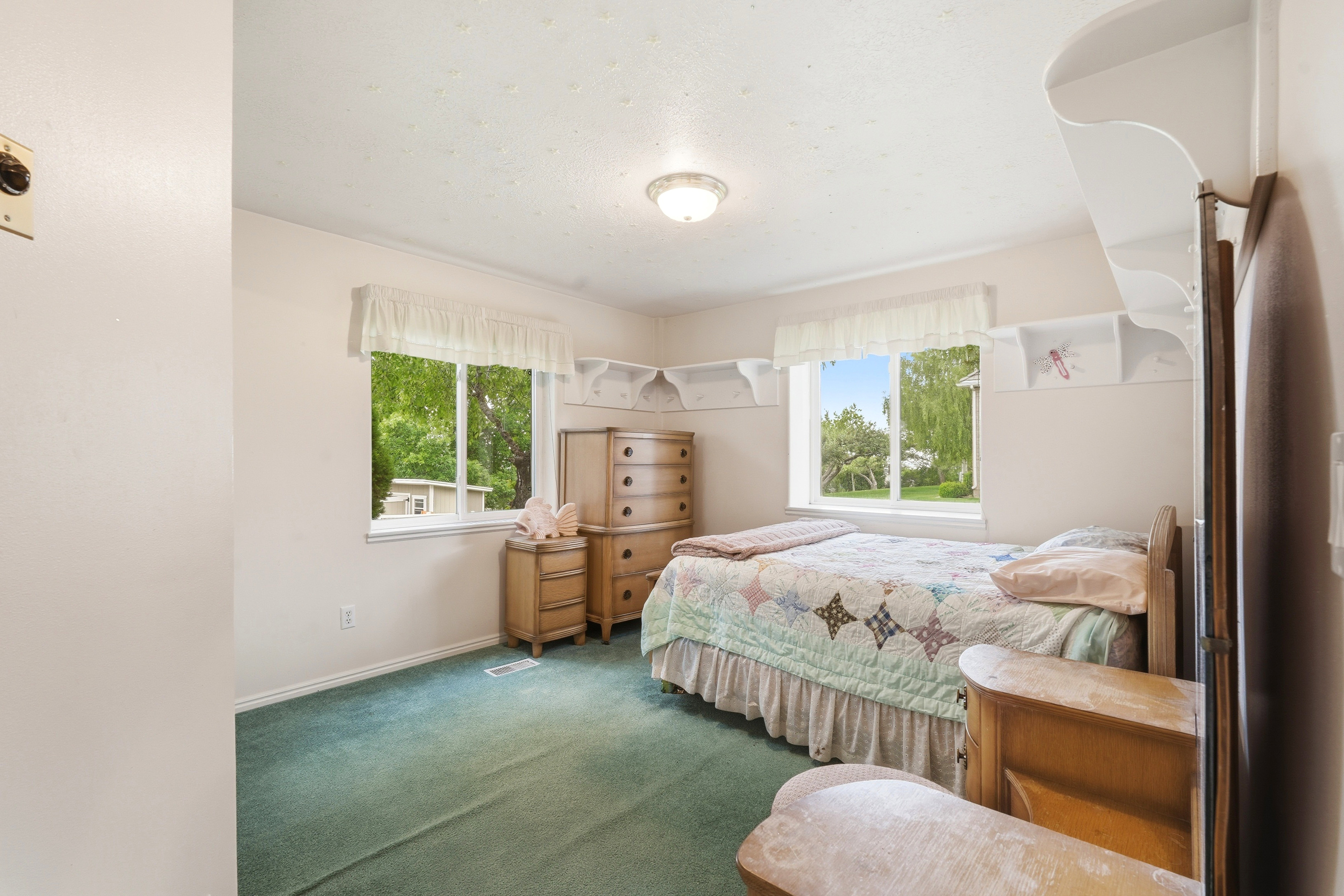 Bedroom featuring two windows, green carpet flooring, recessed wall shelving, and a ceiling-mounted light fixture